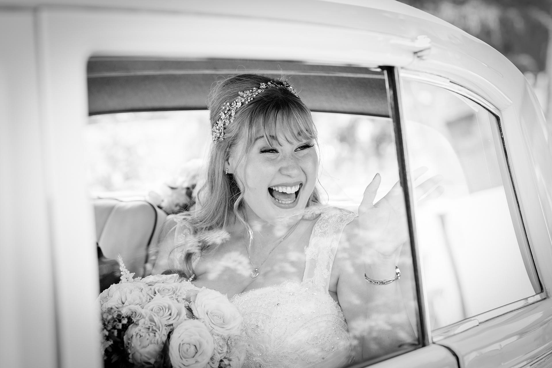 Happy bride waving inside wedding car