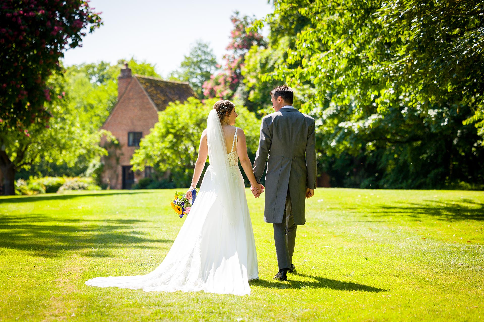 Bride and groom walking through the grounds during a summer wedding at Leez Priory, Great Leighs, Chelmsford, by Essex wedding photographer