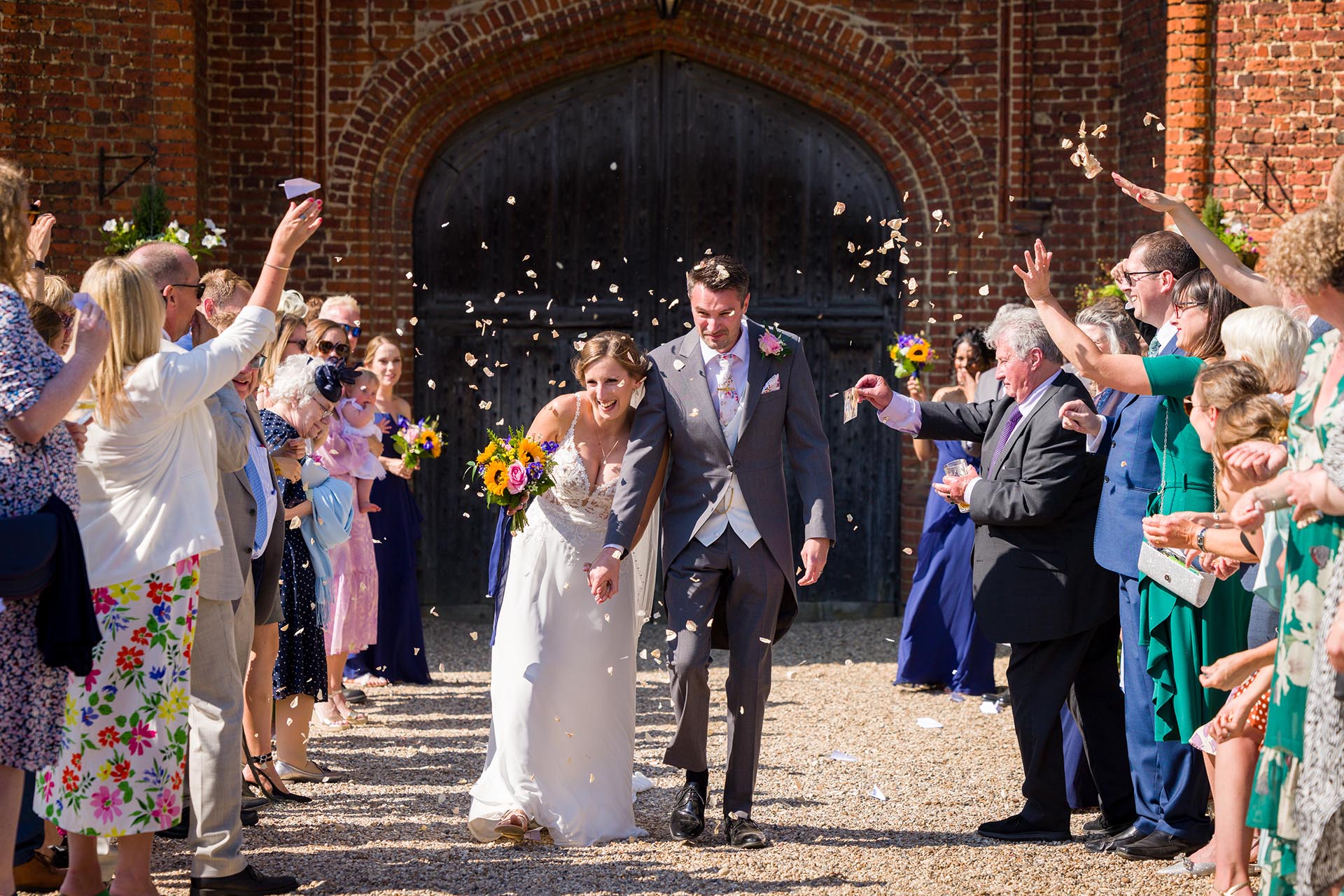 Bride and groom laughing as wedding guests throw confetti at Leez Priory, Great Leighs, Chelmsford