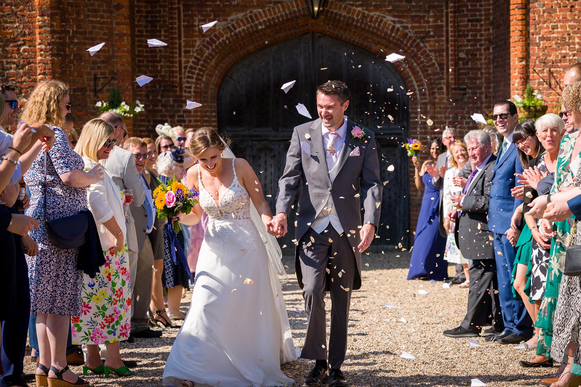 Bride and groom laughing as wedding guests throw confetti at Leez Priory, Great Leighs, Chelmsford, by Essex wedding photographer