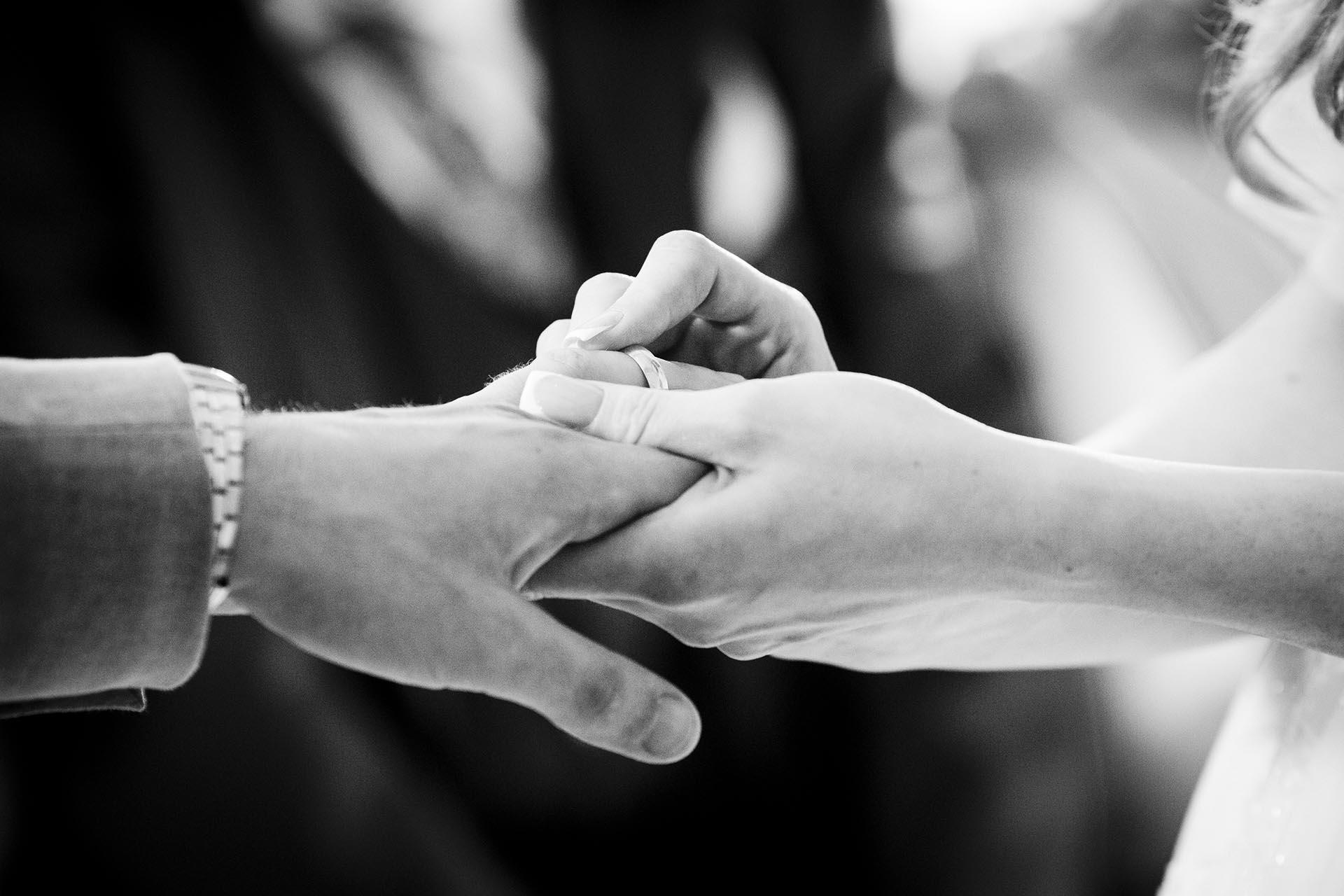 Close up black and white photograph of a wedding ring being put on during the ceremony at Apton Hall, Rochford, Essex