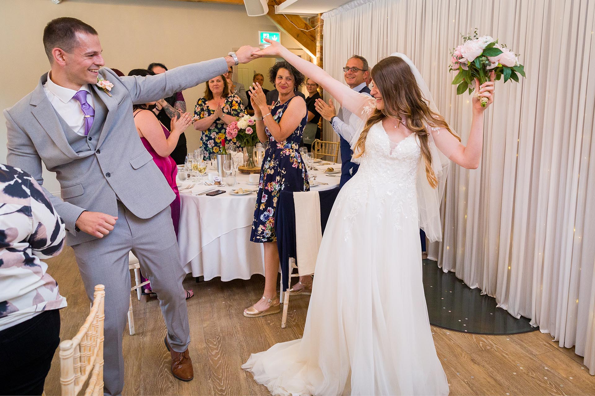 Photograph of bride and groom dancing into their reception with wedding guests cheering at Apton Hall, Rochford, Essex