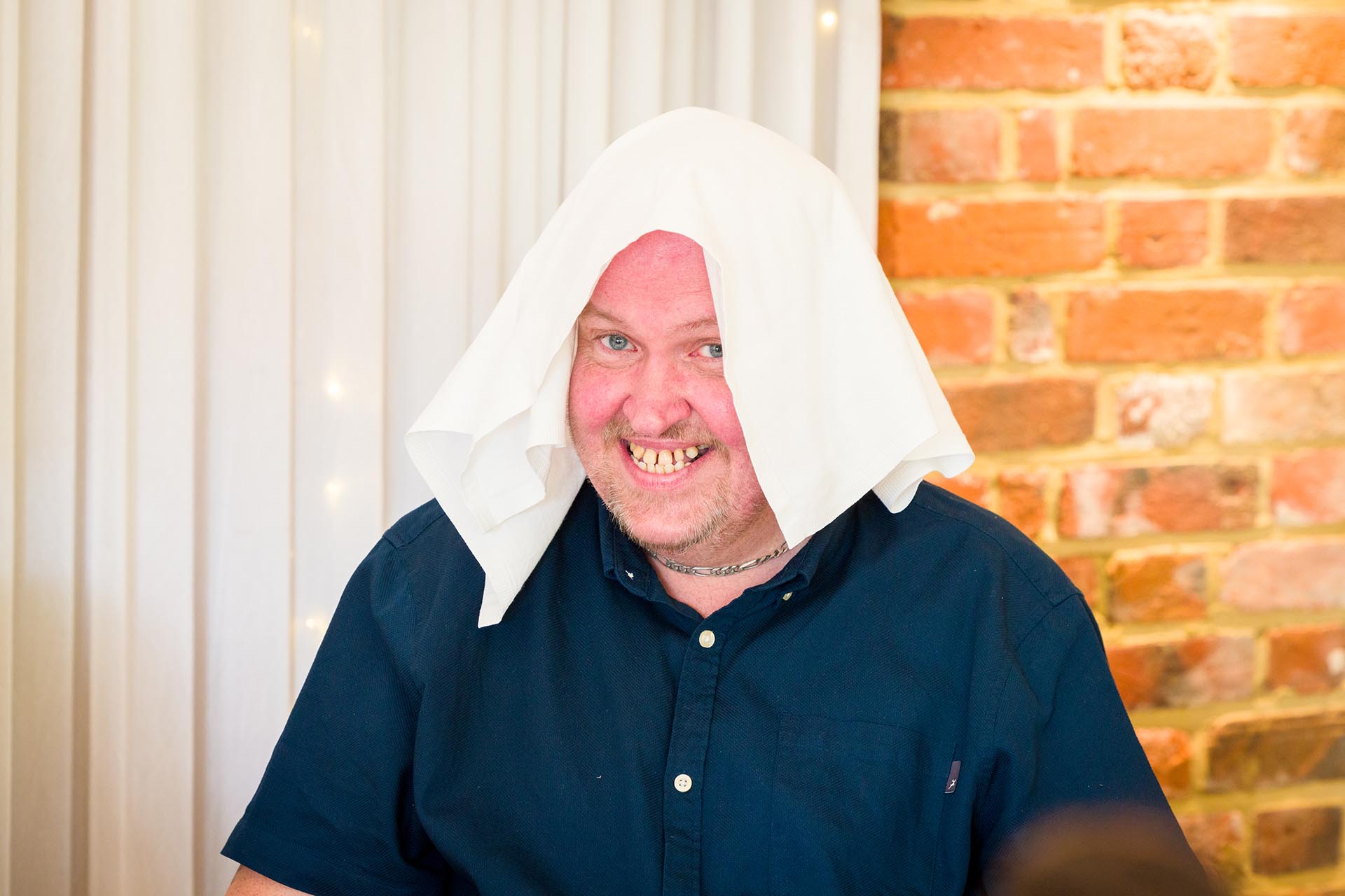 Photograph of wedding guest laughing with a napkin on his head at Apton Hall, Rochford, Essex