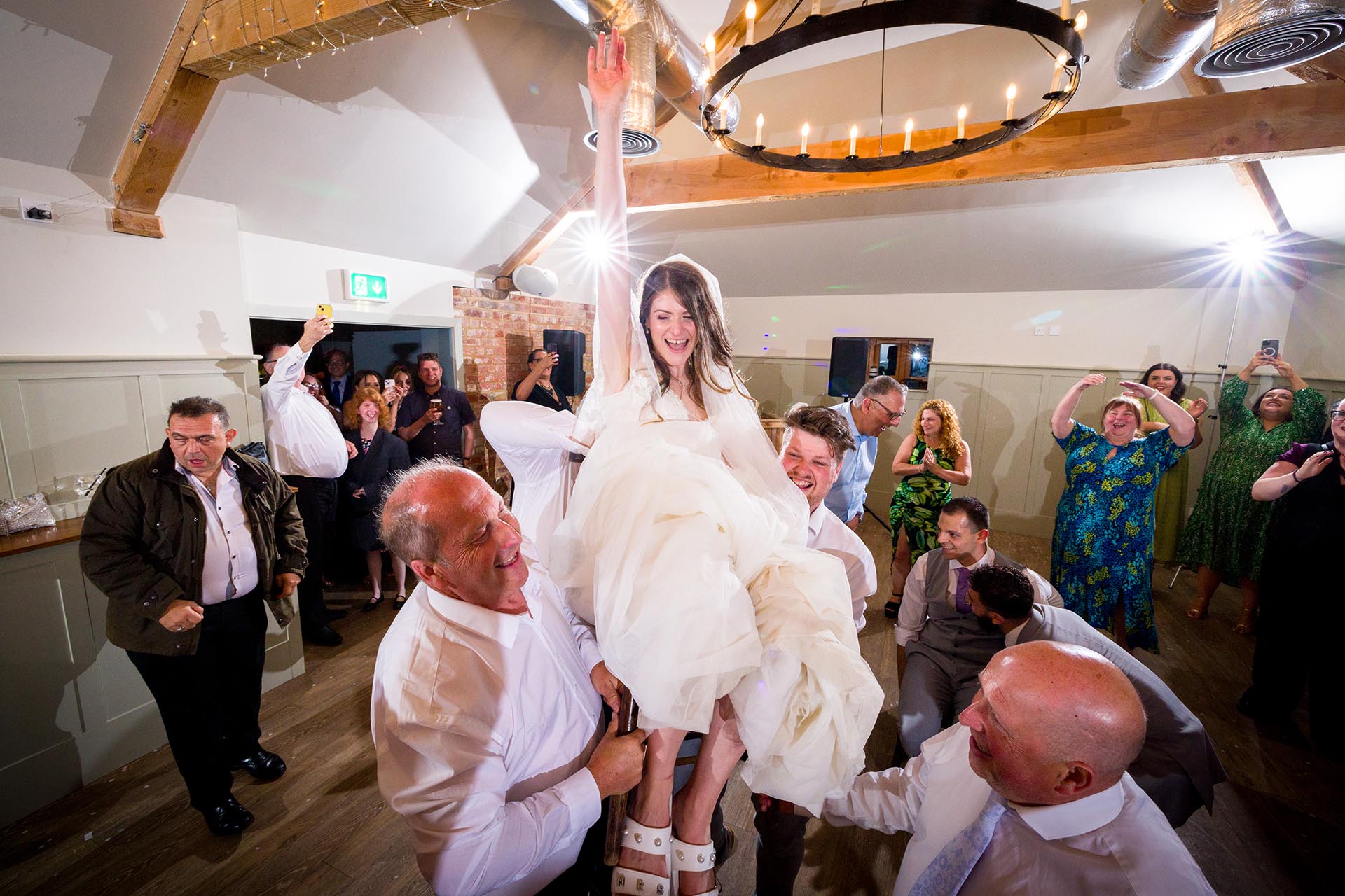 Colourful photograph of bride being lifted on chair whilst dancing at Apton Hall, Rochford, Essex