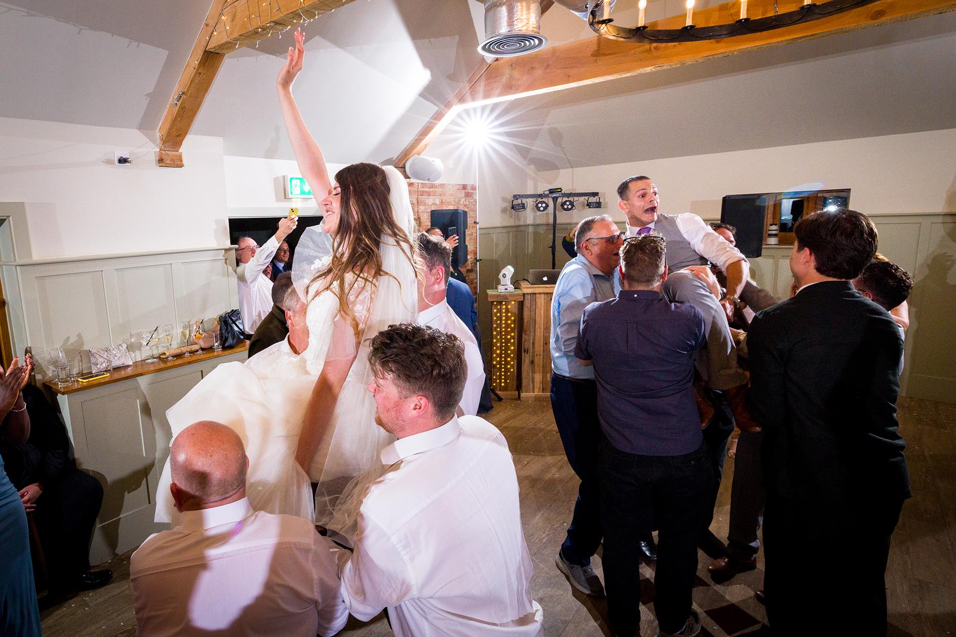Colourful photograph of bride and groom being lifted on chairs whilst dancing at Apton Hall, Rochford, Essex