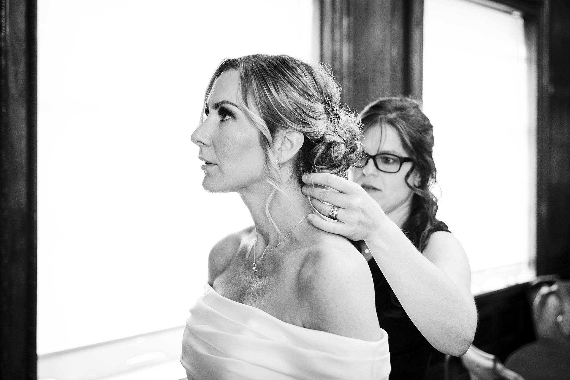 Black and white photograph of bridesmaid helping bride to prepare for wedding