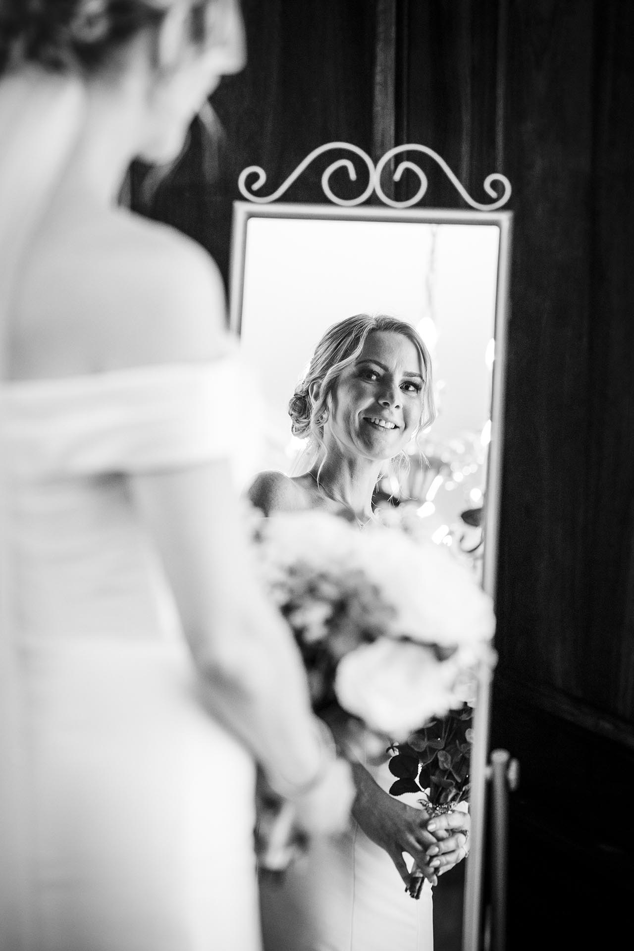 Black and white photograph of bride looking at herself in a mirror before her wedding at Braintree Town Hall, Braintree, Essex