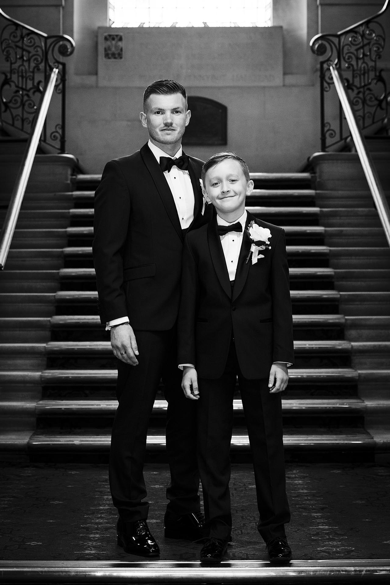 Black and white photograph of groom and young groomsman standing on the staircase at Braintree Town Hall, Braintree, Essex