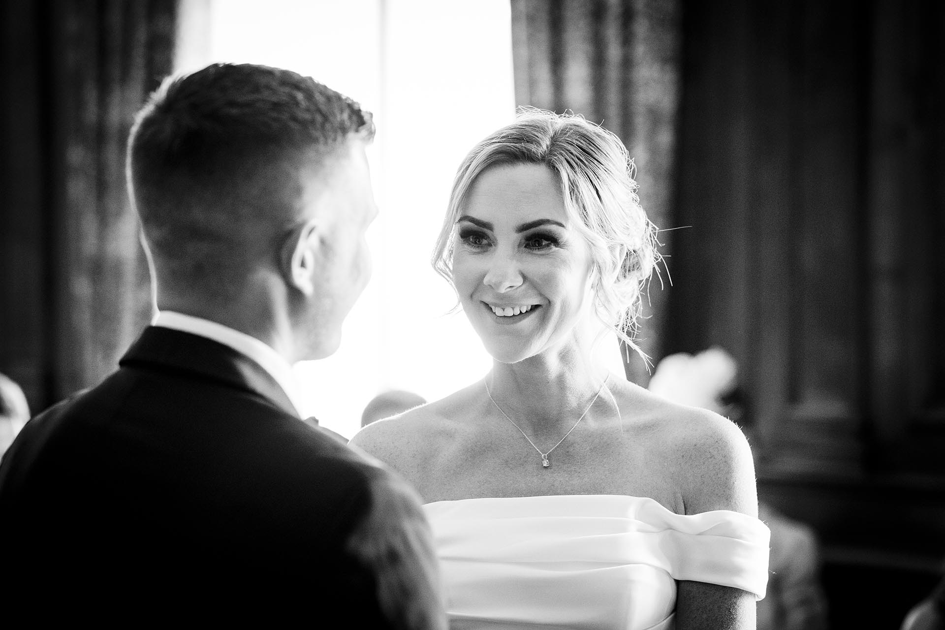 Black and white photograph of bride smiling at her groom during their wedding ceremony at Braintree Town Hall, Braintree, Essex