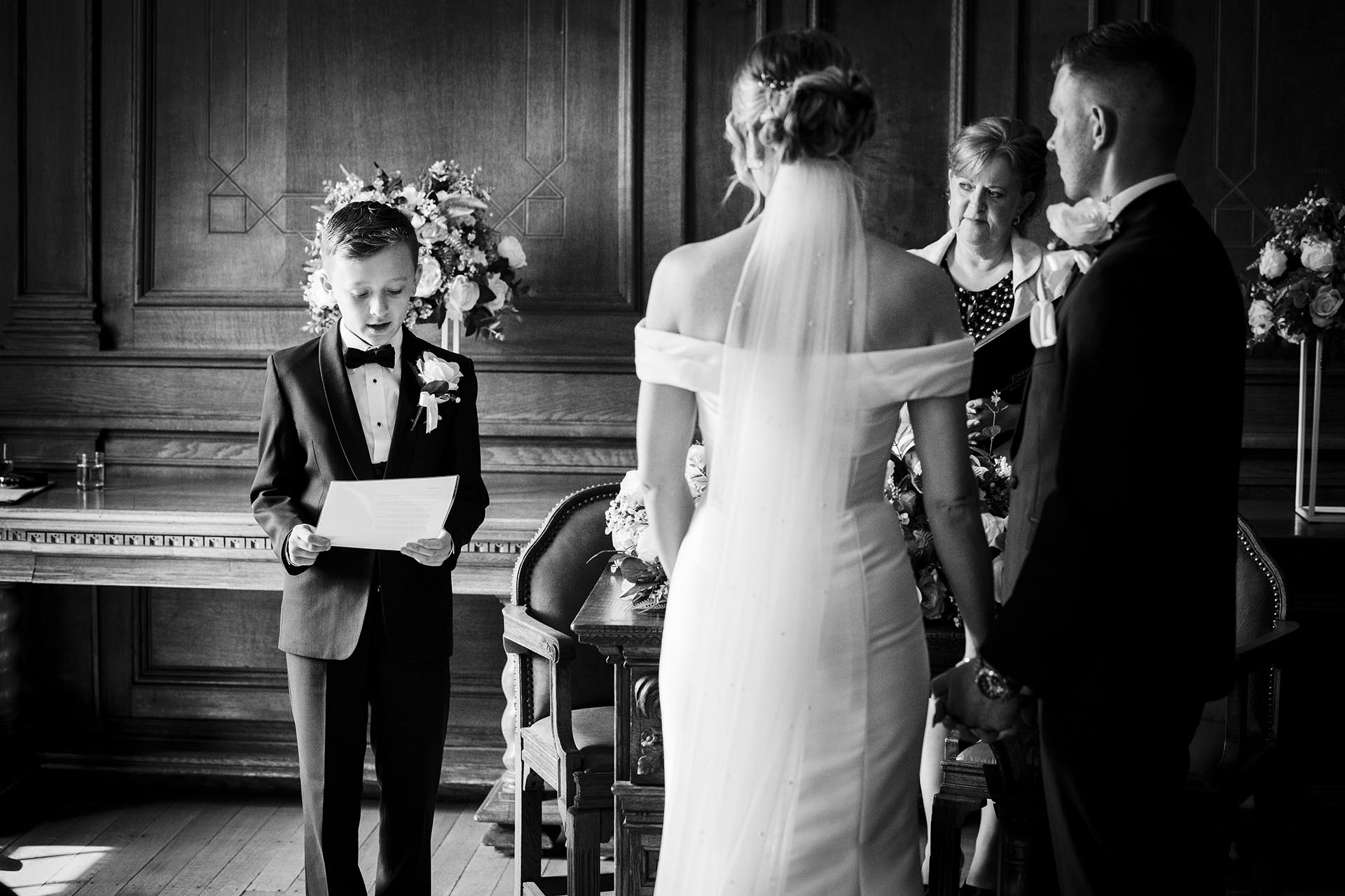 Black and white photograph of young groomsman giving a reading during wedding ceremony at Braintree Town Hall, Braintree, Essex
