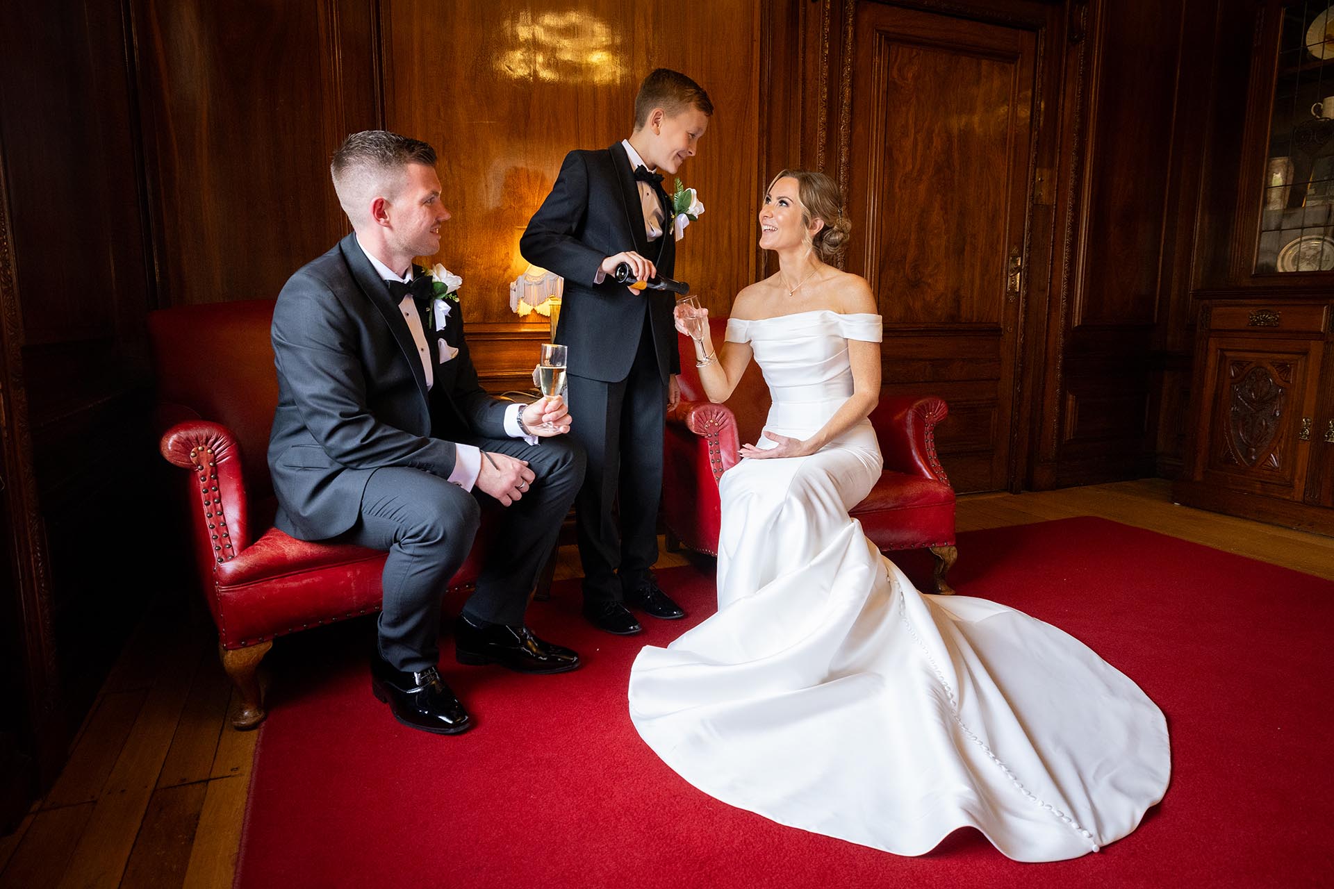 Photograph of a young groomsman pouring a glass of champagne for the bride and groom at Braintree Town Hall, Braintree, Essex