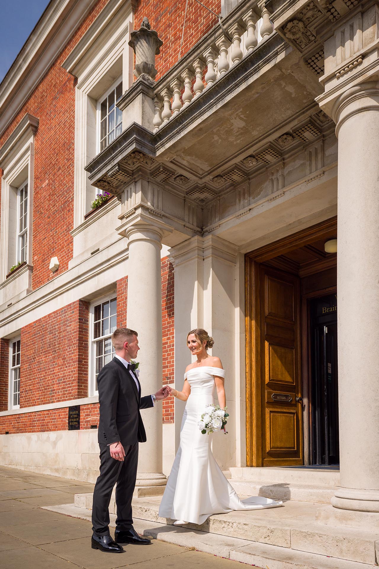 Photograph of the groom helping his bride down the steps outside Braintree Town Hall, Braintree, Essex