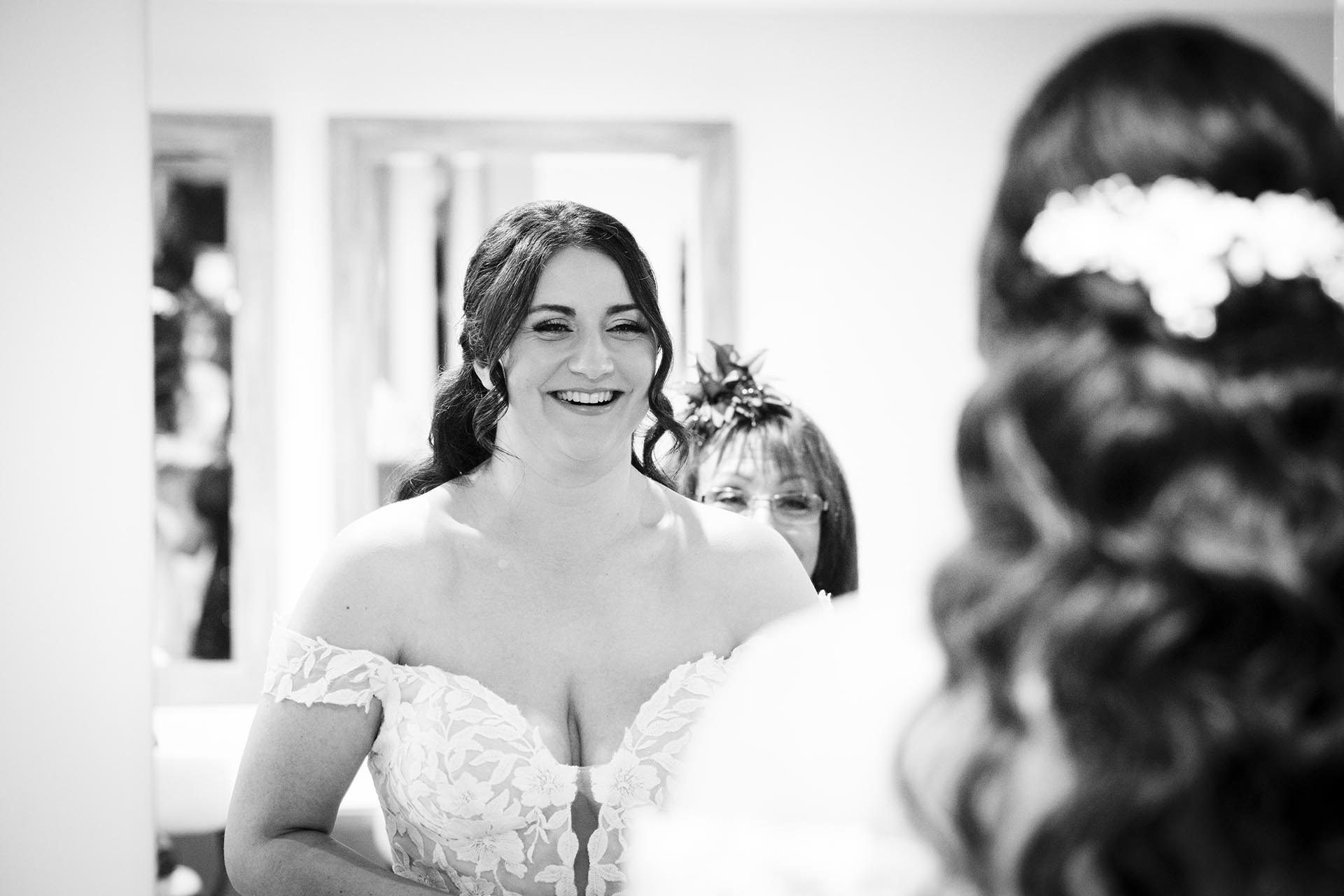 Black and white photograph of bride smiling in a mirror