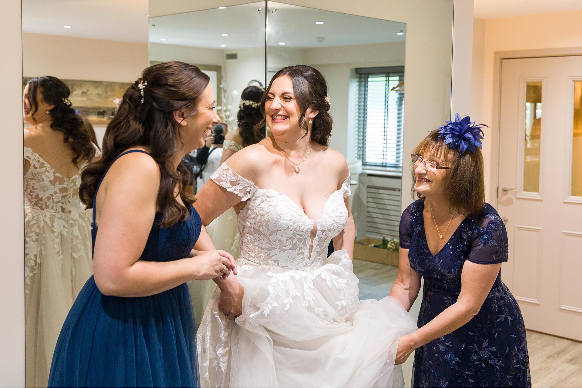 Photograph of bride laughing with her mother and bridesmaid in the bridal room at The Compasses at Pattiswick