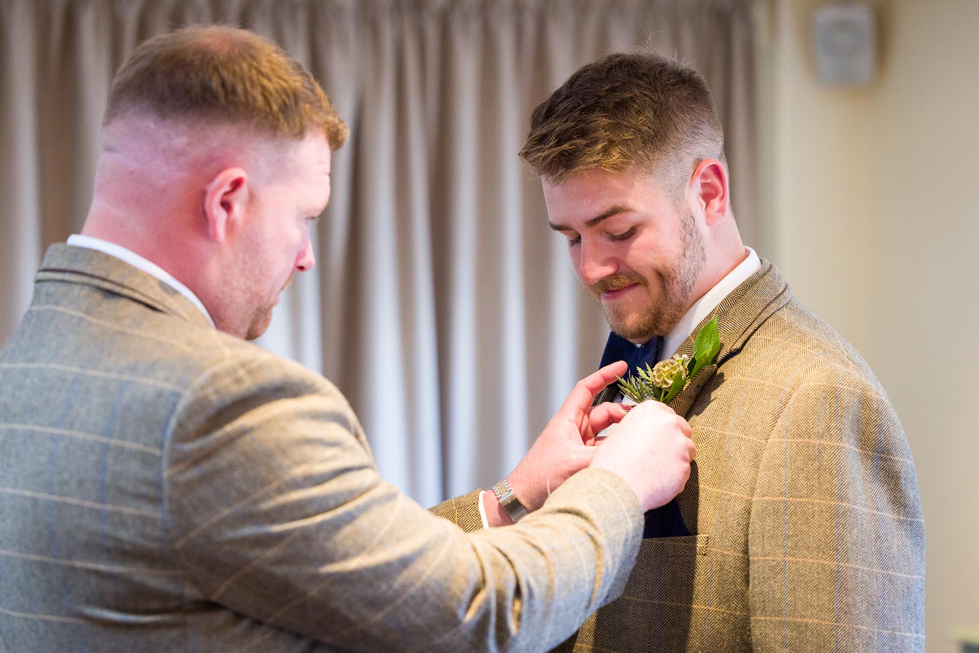 Photograph of best-man fixing button hole flower to groom