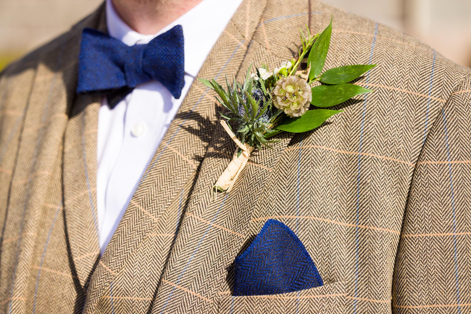 Detail photograph of groom's button-hole flowers, tweed jacket and bow-tie