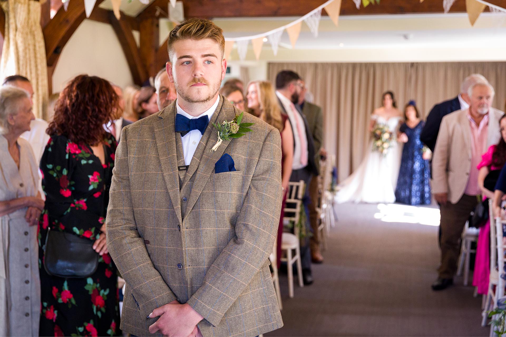 Photograph of groom waiting at the end of the aisle as his bride arrives in the ceremony room at The Compasses at Pattiswick, Essex