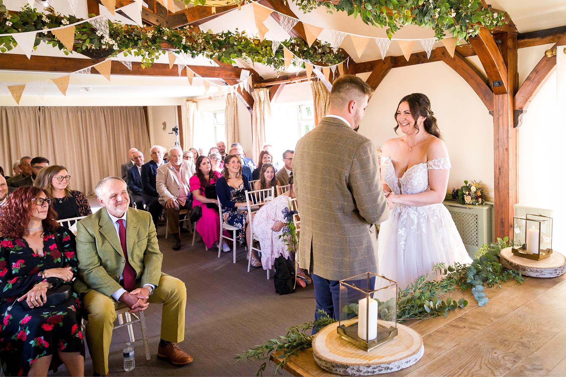 Photograph of bride smiling at her groom infront of wedding guests in the ceremony room at The Compasses at Pattiswick, Essex
