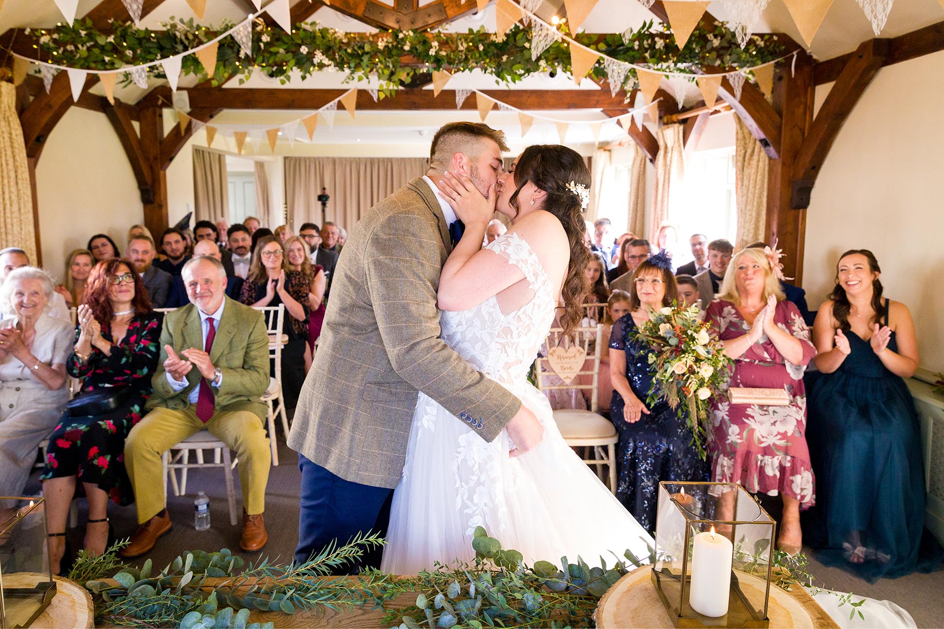 Photograph of bride and groom kissing infront of applauding wedding guests in the ceremony room at The Compasses at Pattiswick, Essex