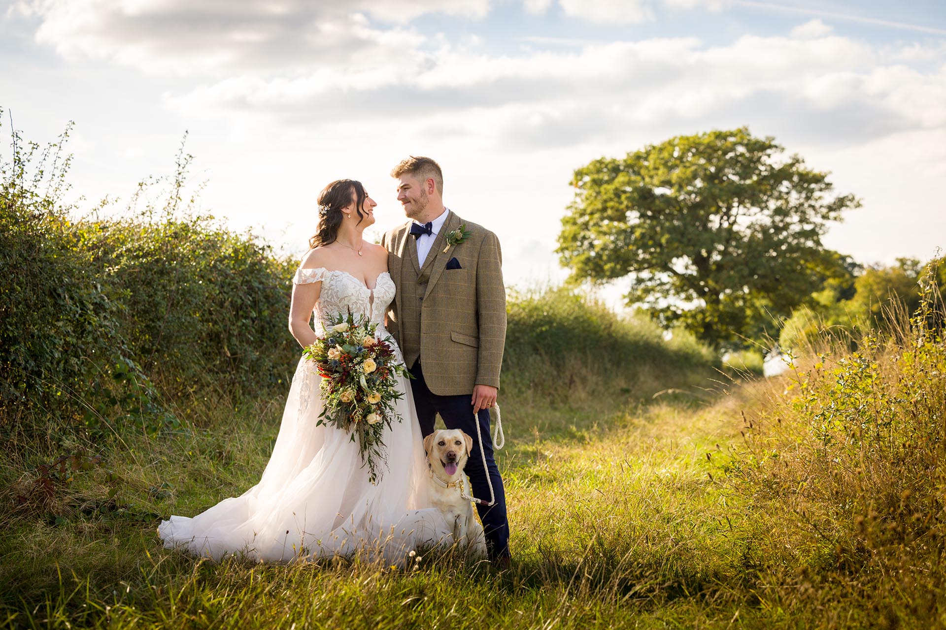 Photograph of bride and groom with their labrador dog in a field near The Compasses at Pattiswick