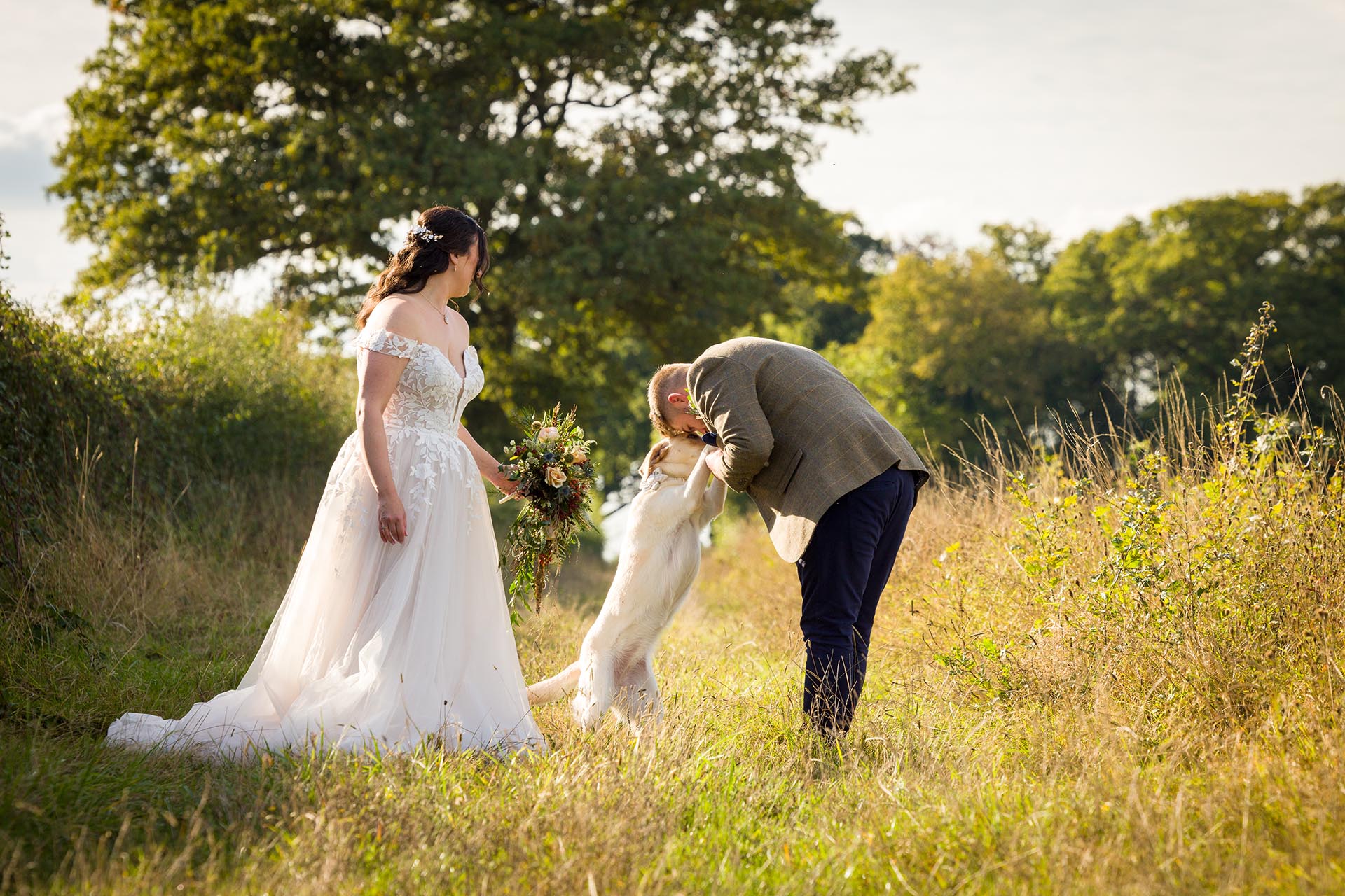 Photograph of bride and groom with their labrador dog in a field near The Compasses at Pattiswick
