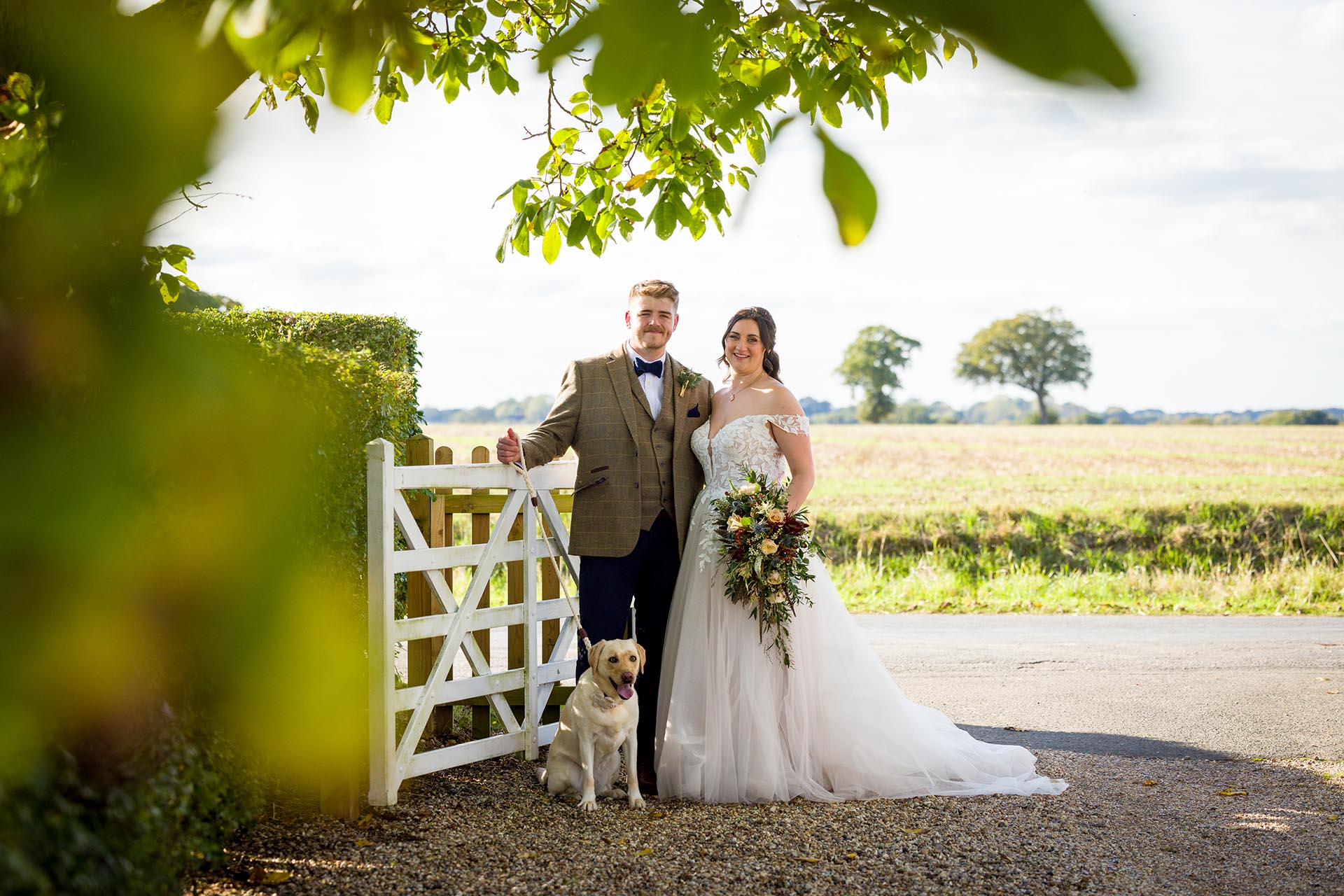 Photograph of bride and groom with their labrador dog at the white gate at The Compasses at Pattiswick