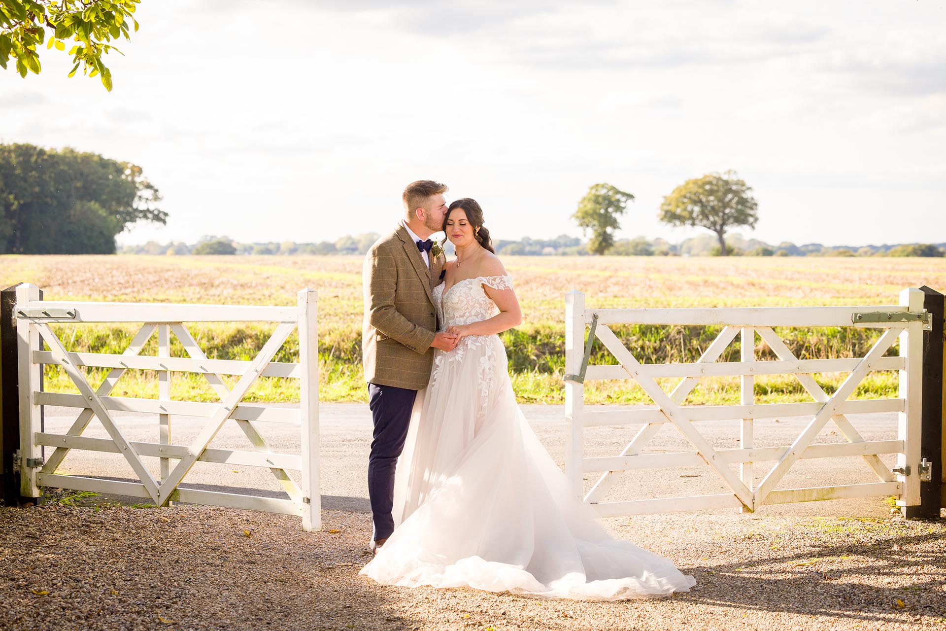 Photograph of bride and groom kissing infront of the white gates at The Compasses at Pattiswick