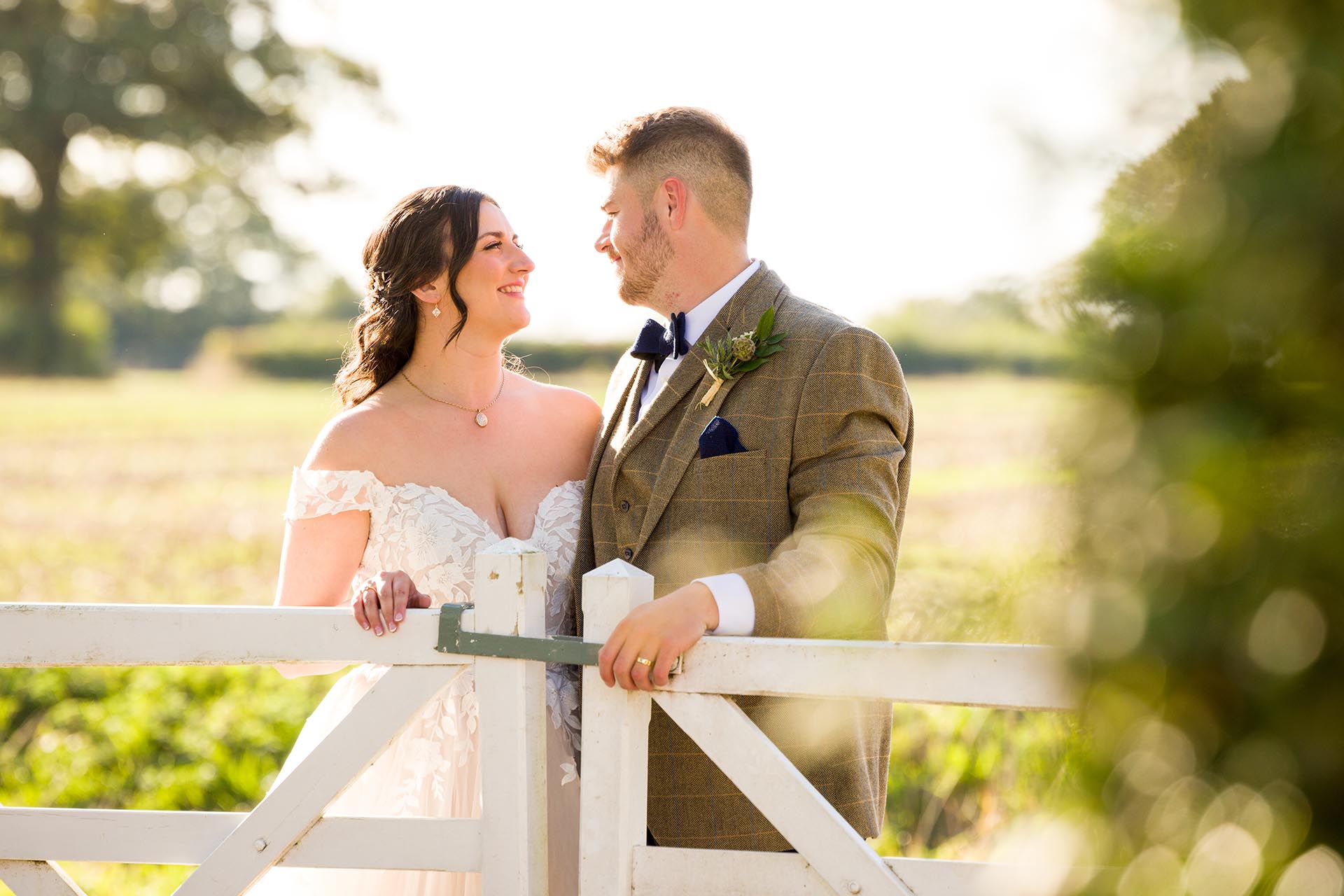 Photograph of bride and groom leaning on the white gates at The Compasses at Pattiswick