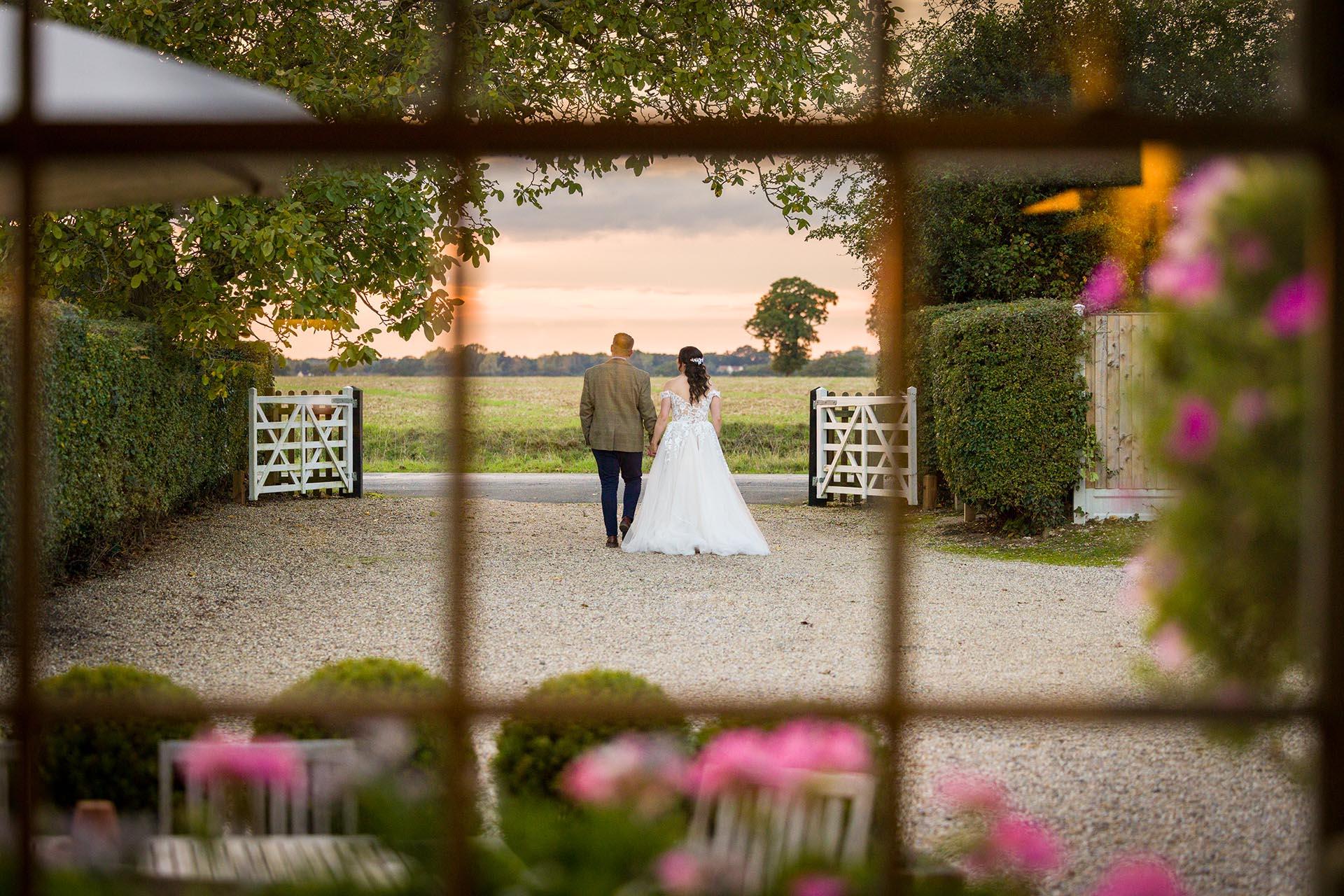 Photograph through a window of bride and groom going for a walk at The Compasses at Pattiswick