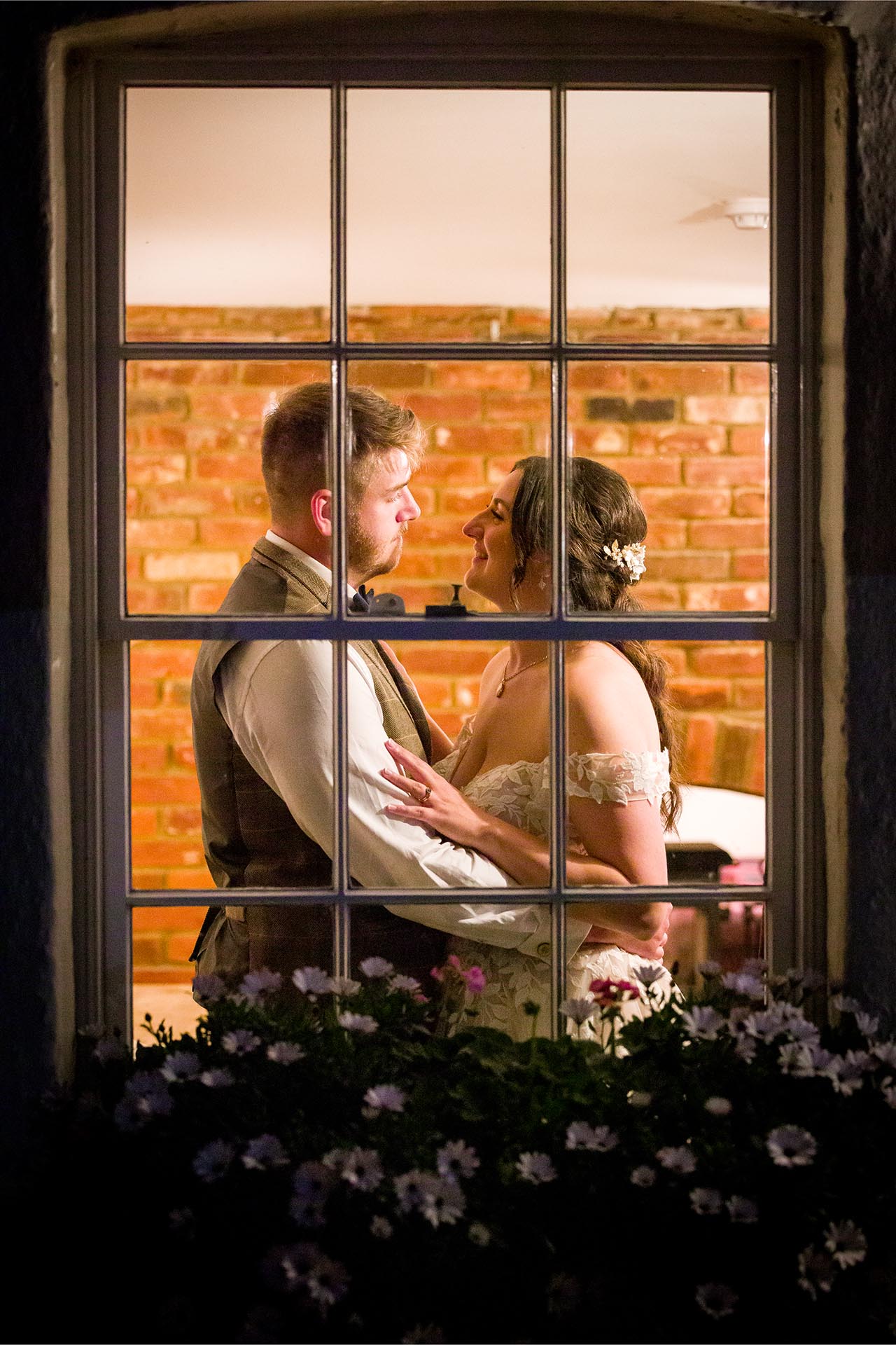 Photograph looking through a window of bride and groom hugging inside The Compasses at Pattiswick