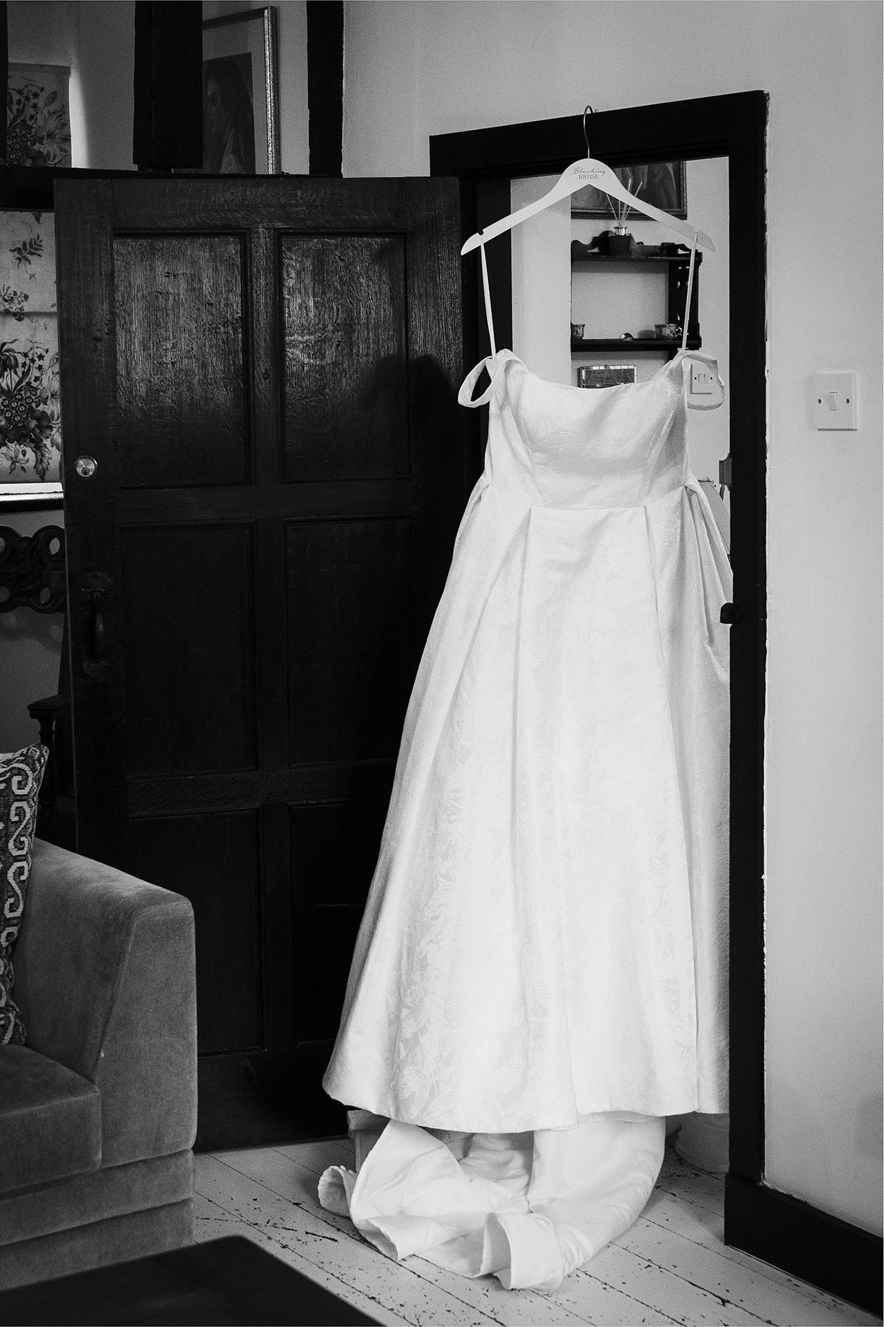 Black and white photograph of bride's wedding dress hanging in a doorway
