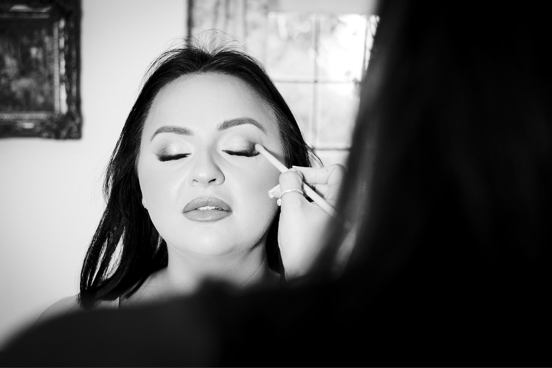 Black and white photograph of bride having eye make-up applied