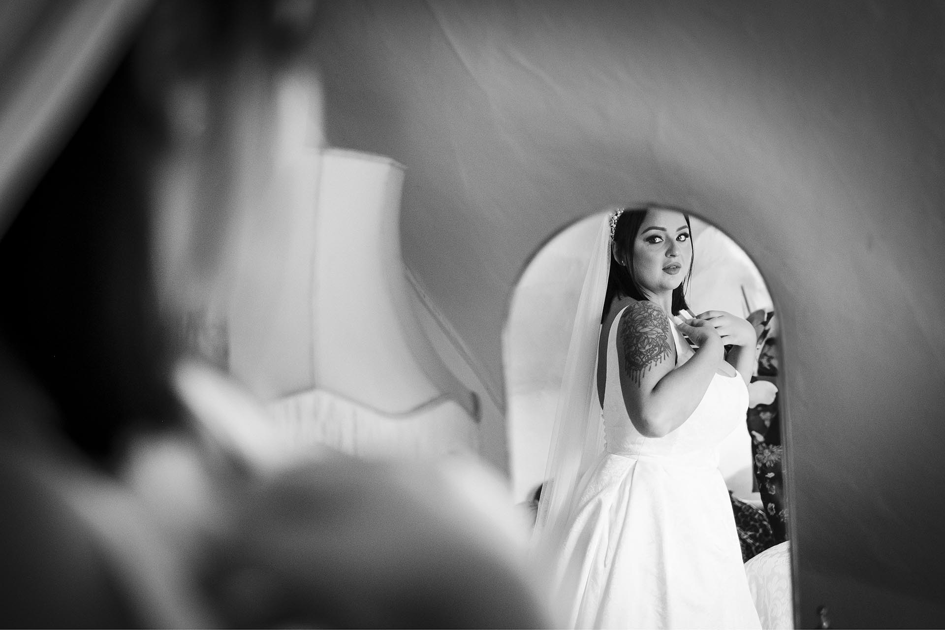 Black and white photograph of bride looking at herself in a mirror