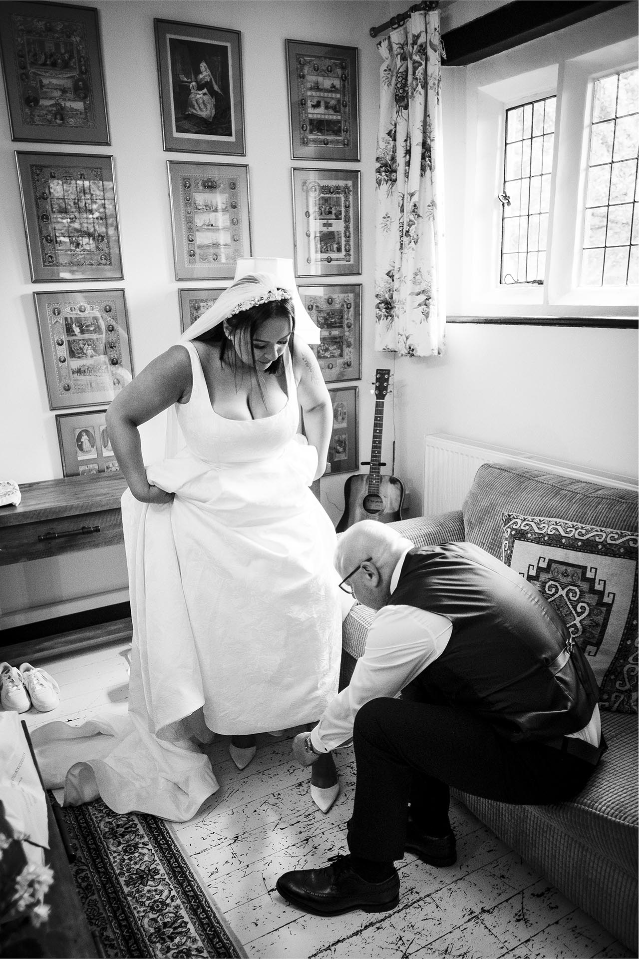 Black and white photograph of bride's father fastening her shoes