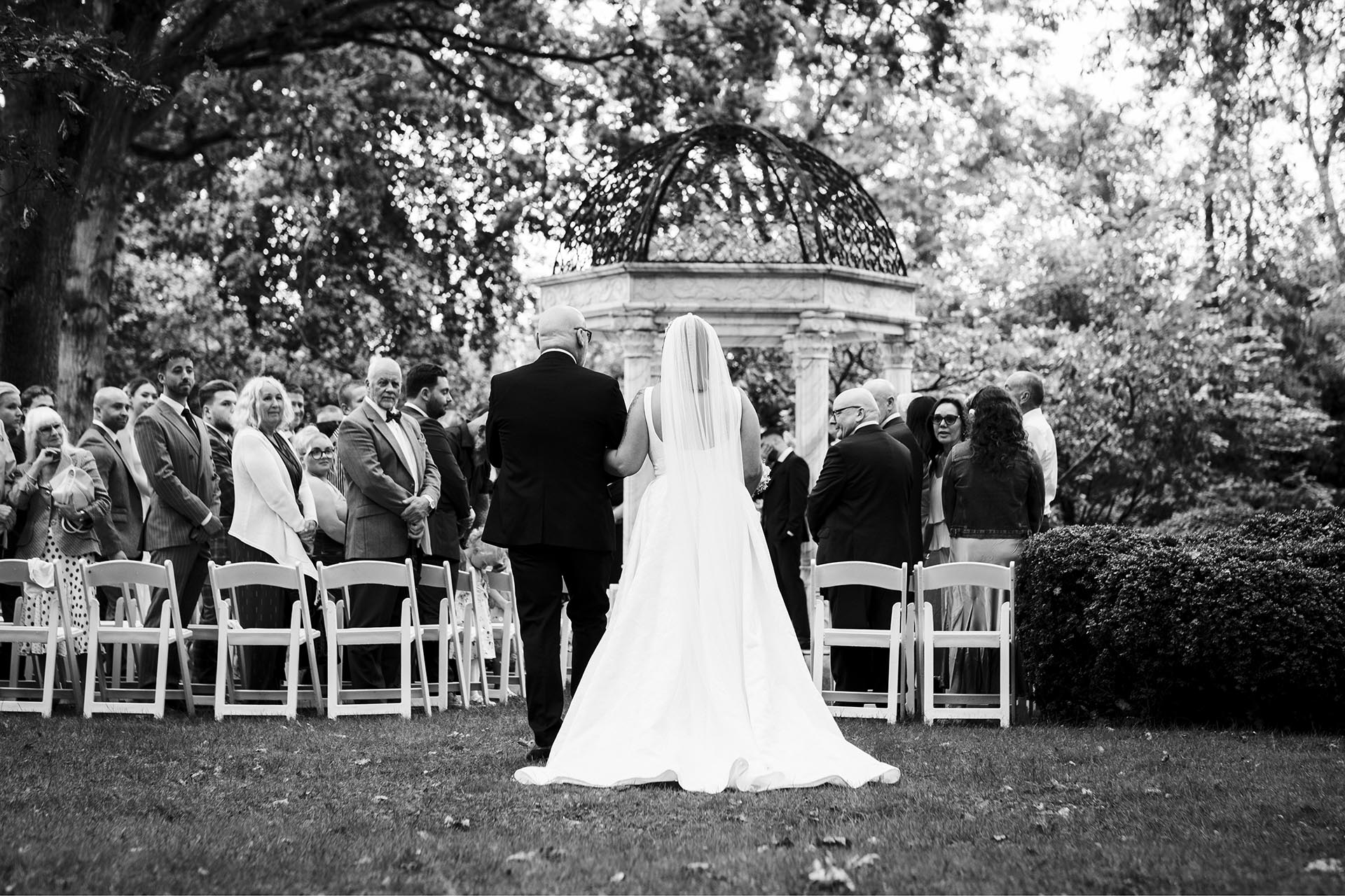 Black and white photograph of bride walking down the aisle with her father for outdoor wedding ceremony