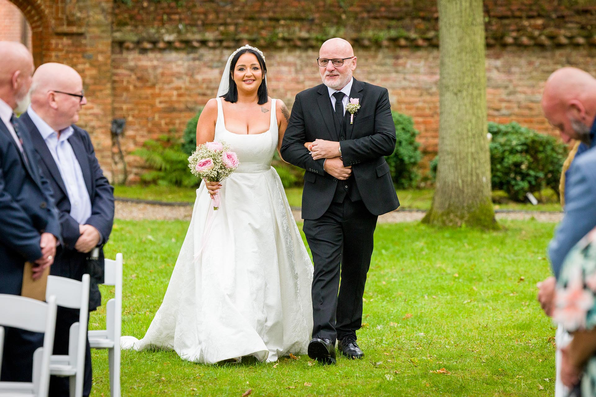 Photograph of bride walking down the aisle with her father for outdoor wedding ceremony