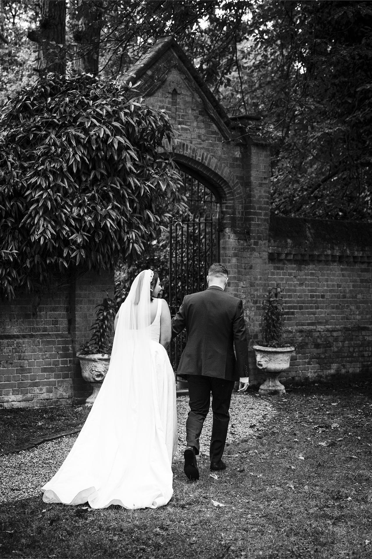 Black and white photograph of bride and groom walking towards brick arch at Creeksea Place Manor
