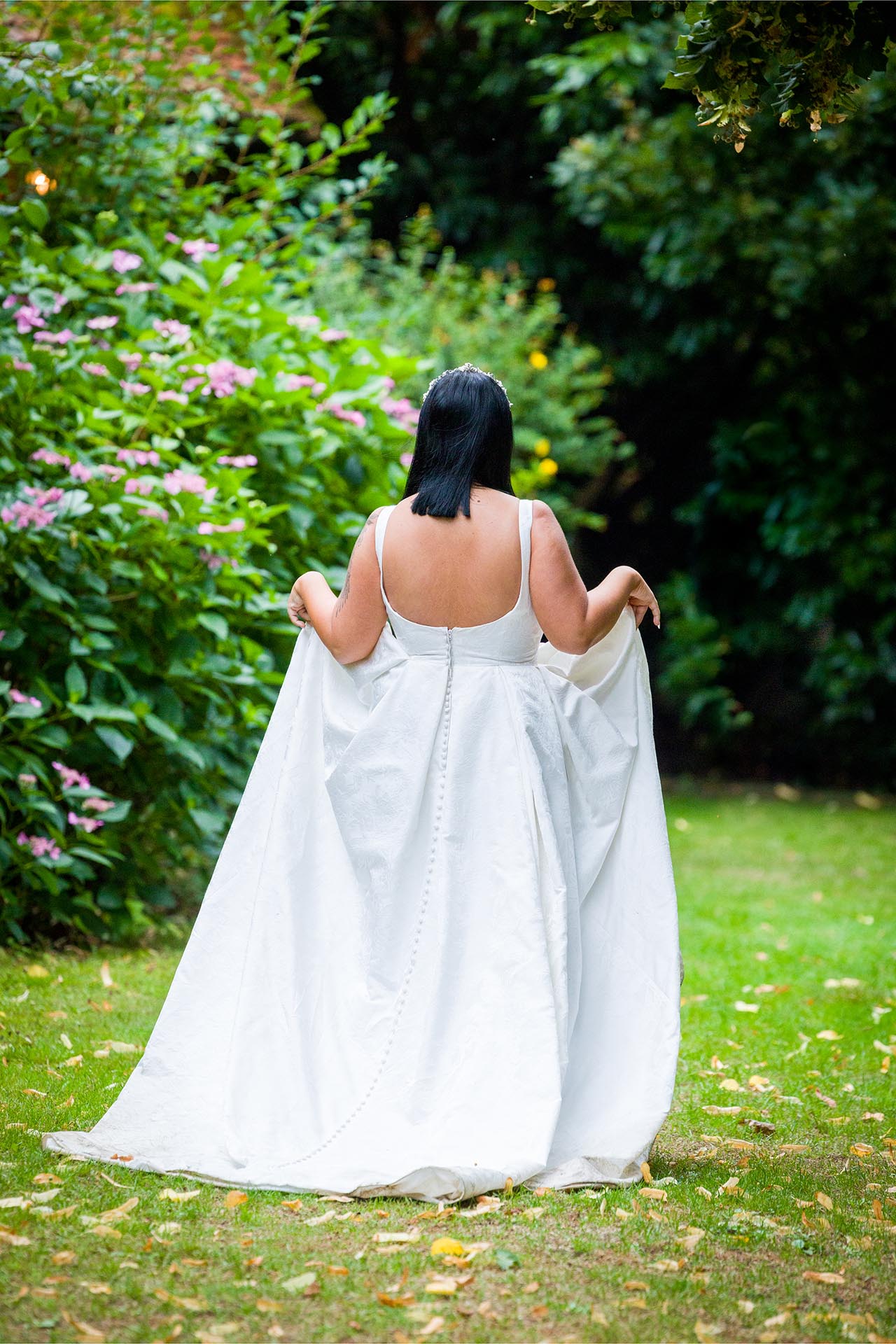 Photograph of bride trying to keep her dress dry as she walks across grass