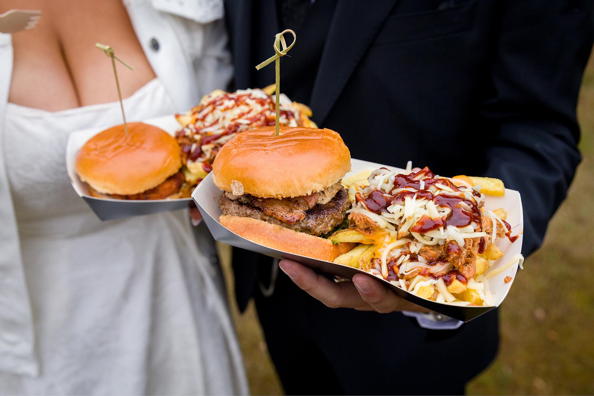 Close up Photograph of burgers and chips being held by bride and groom