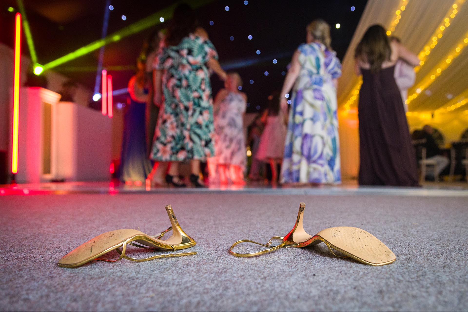Photograph of wedding guests shoes on floor with dancers in the background