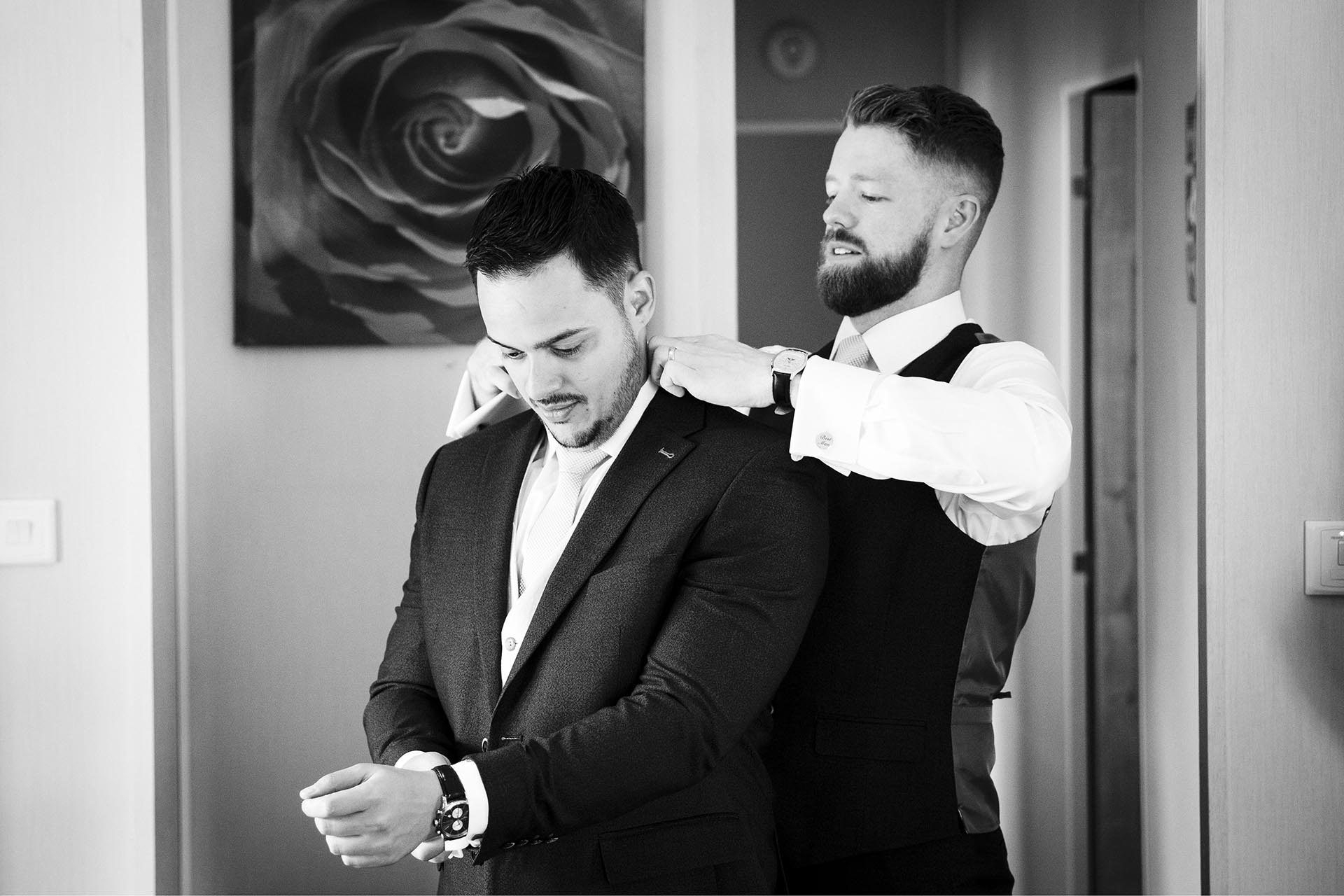 Black and white photograph of the best man straightening the groom's collar