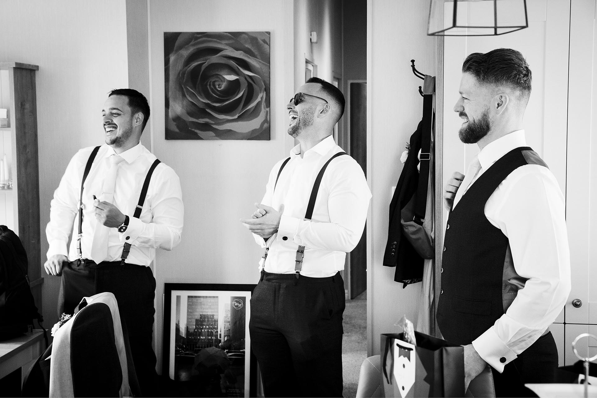 Black and white photograph of the grrom and two groomsmen laughing