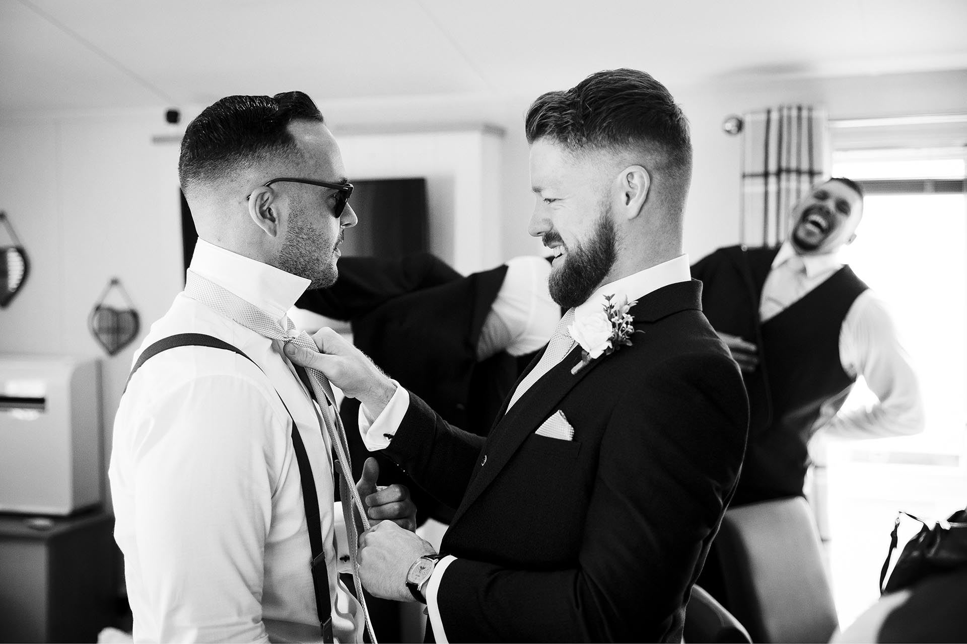 Black and white photograph of groomsmen helping with each other's ties