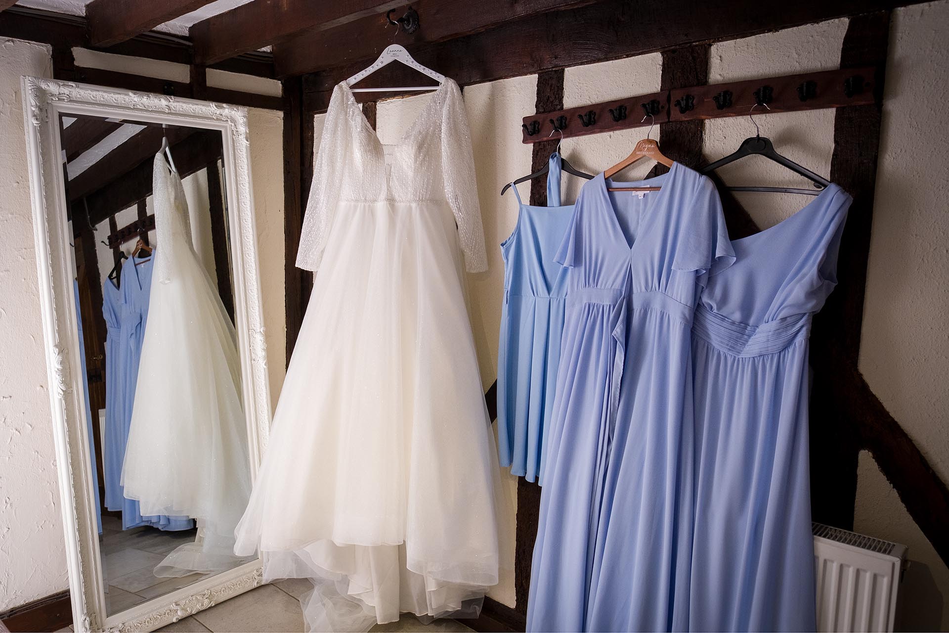 Photograph of a bridal wedding dress hanging up alongside three bridesmaid's dresses