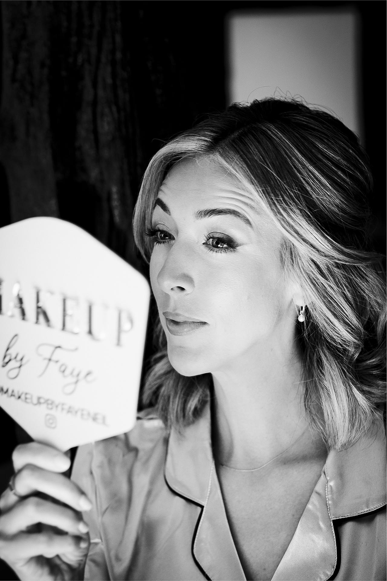 Black and white photograph of a bridesmaid checking her make-up in a hand mirror