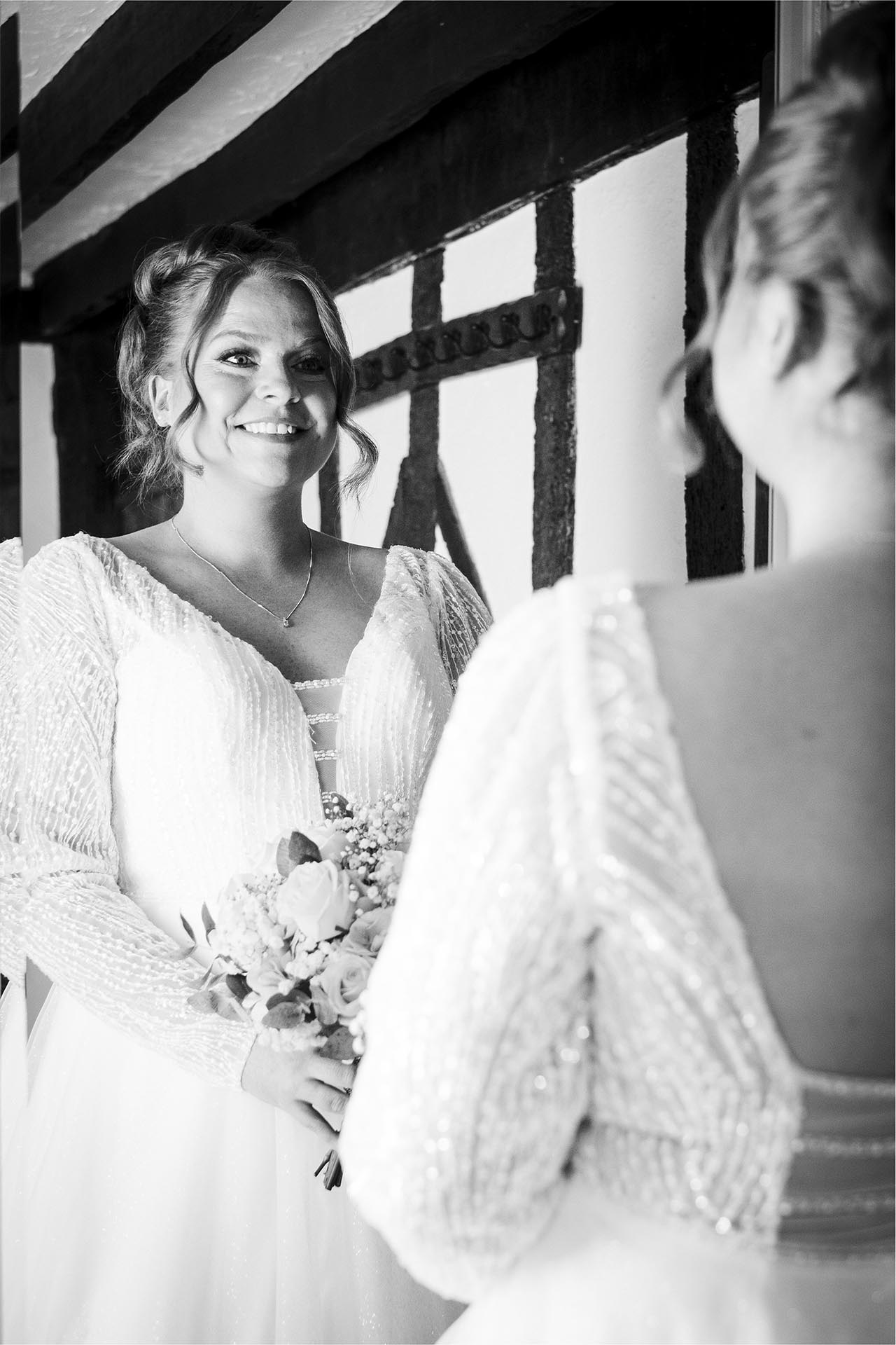 Black and white photograph of bride smiling at herself in a mirror