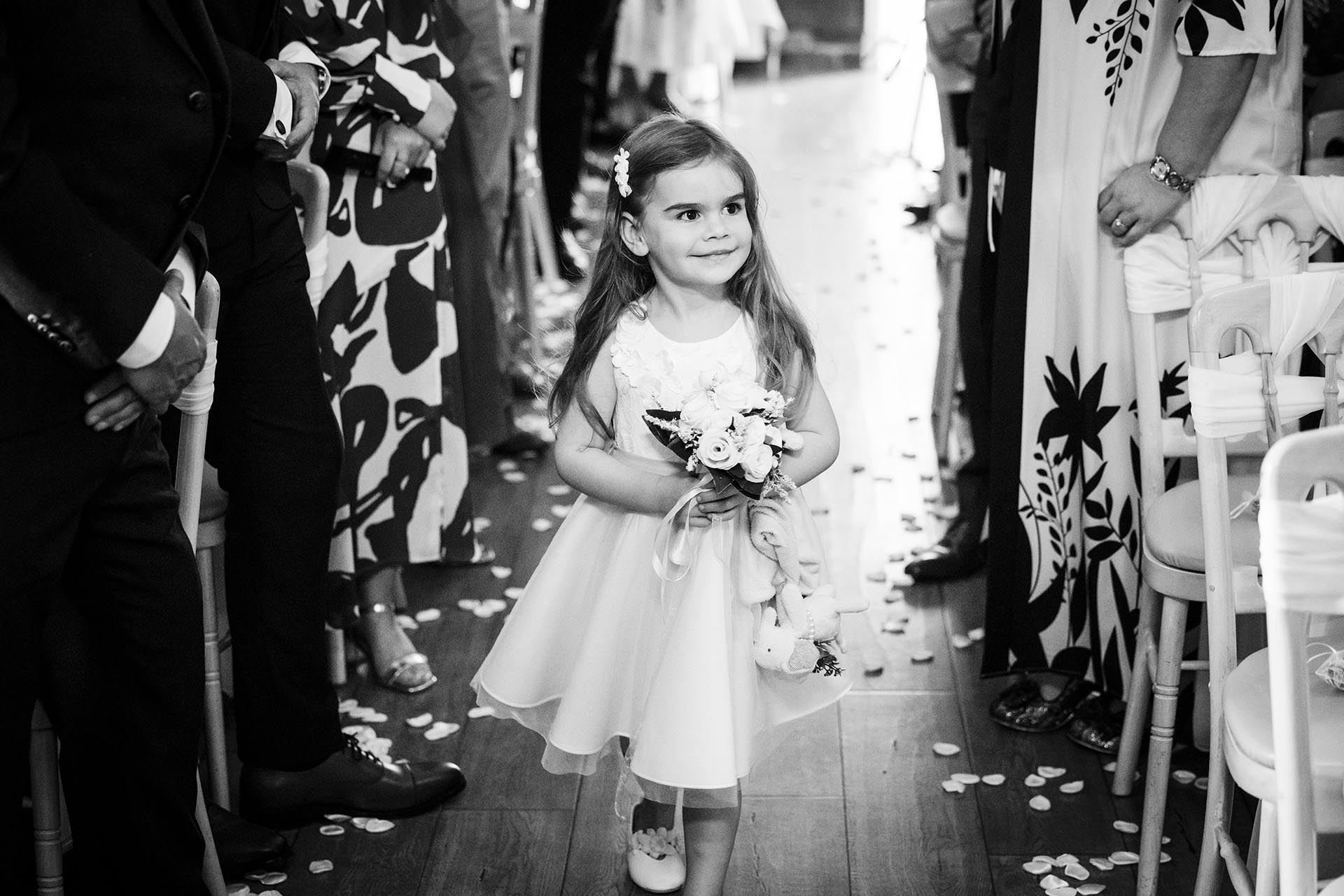 Black and white photograph of a young flower girl walking down the aisle