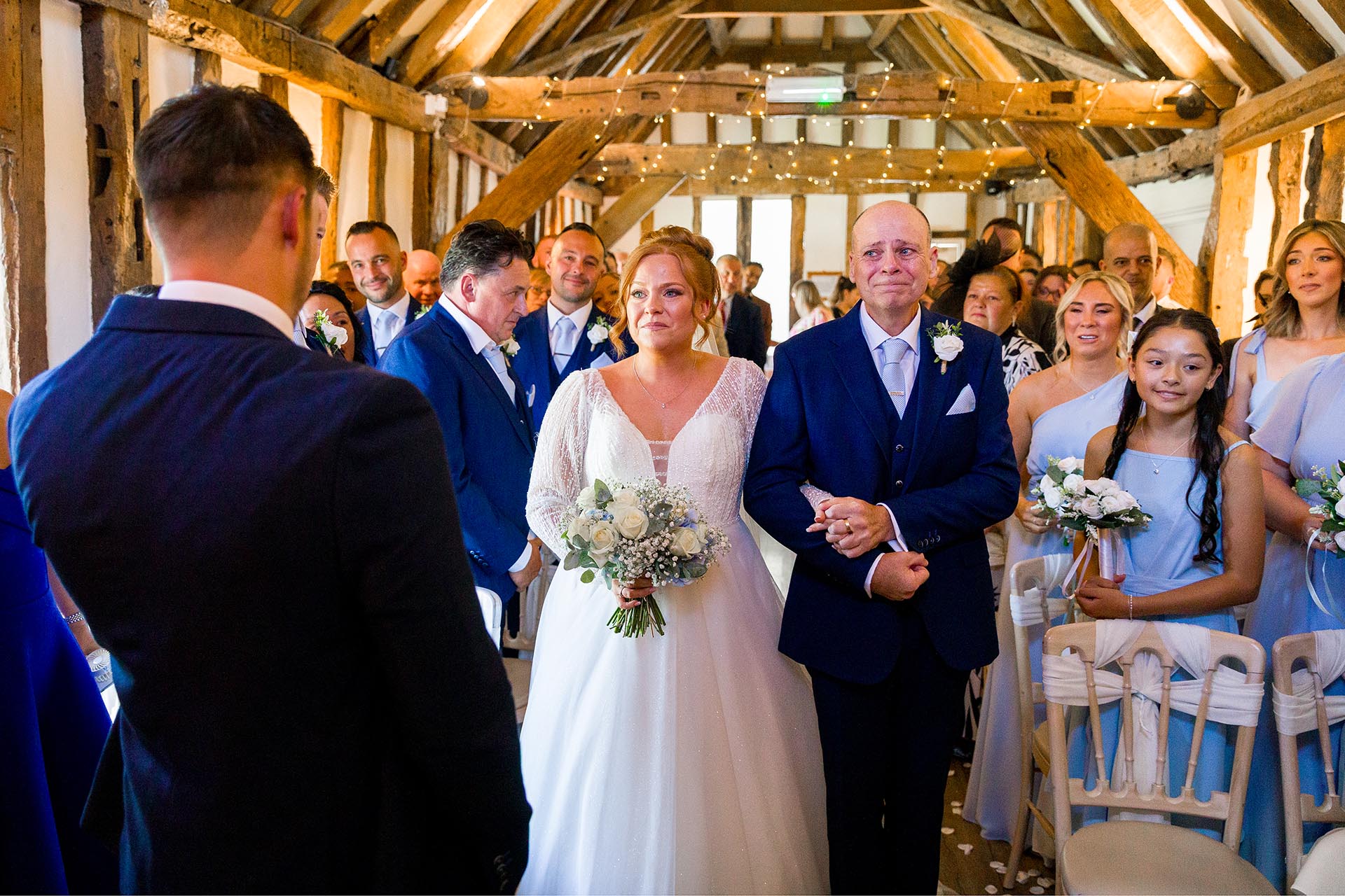 A bride smiling at her groom whilst walking down the aisle with her father