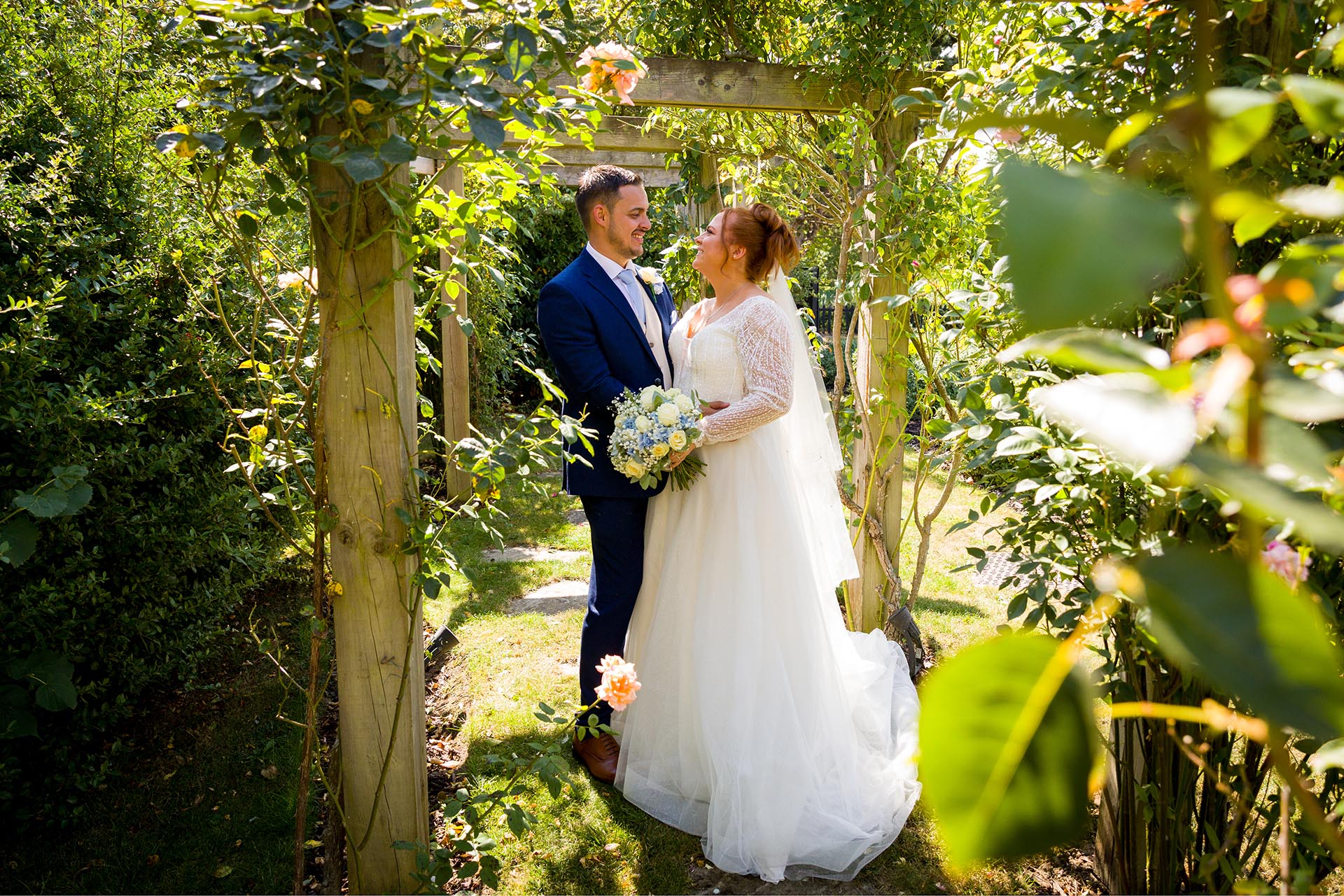 Bride and groom smiling at each other under a rose arch at Little Channels, Essex