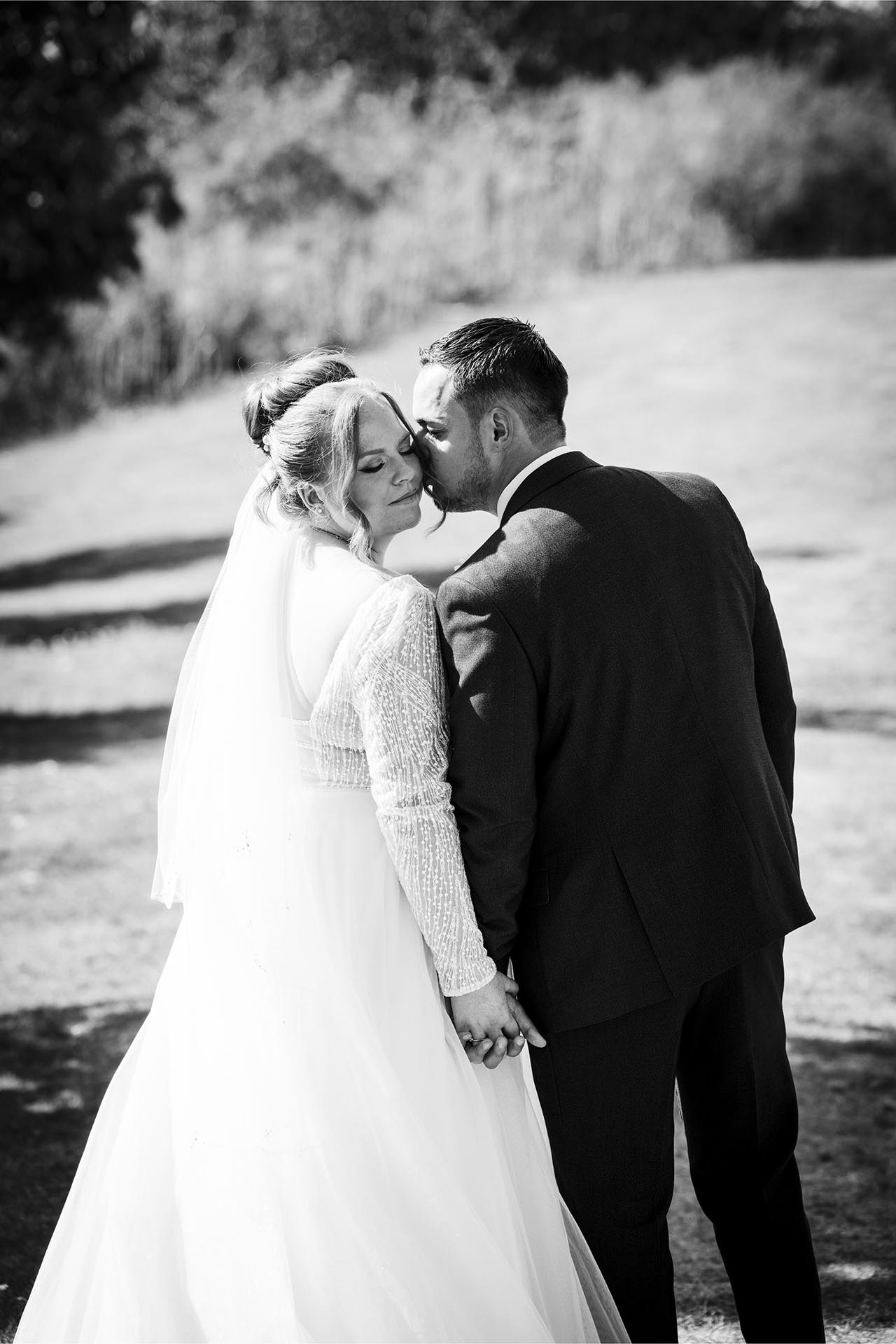 Black and white photograph of Groom kissing his bride